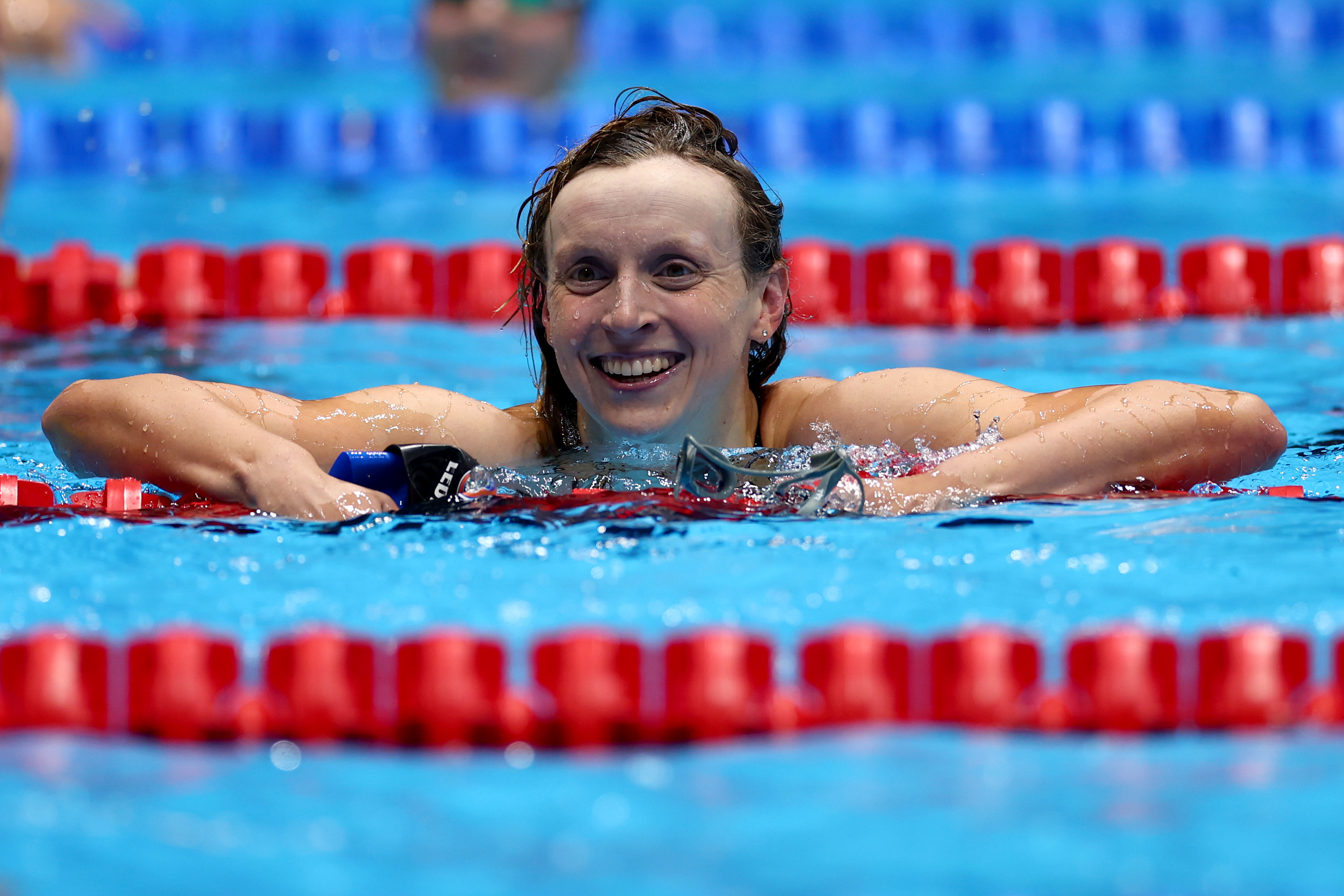 Katie Ledecky smiling while resting on the lane divider in a swimming pool after a race