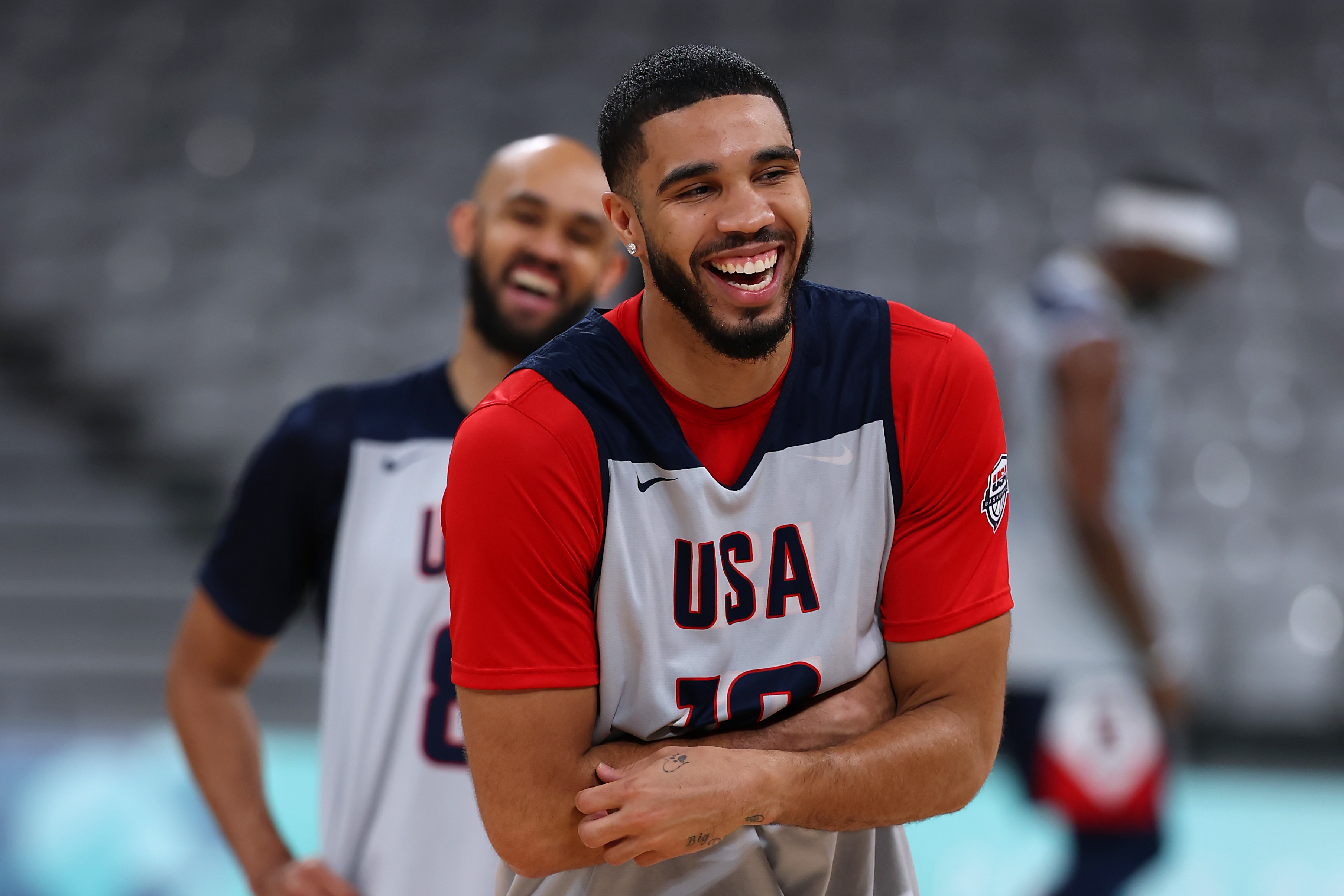 Jayson Tatum and a teammate, dressed in USA basketball jerseys, are smiling and standing on a basketball court during practice