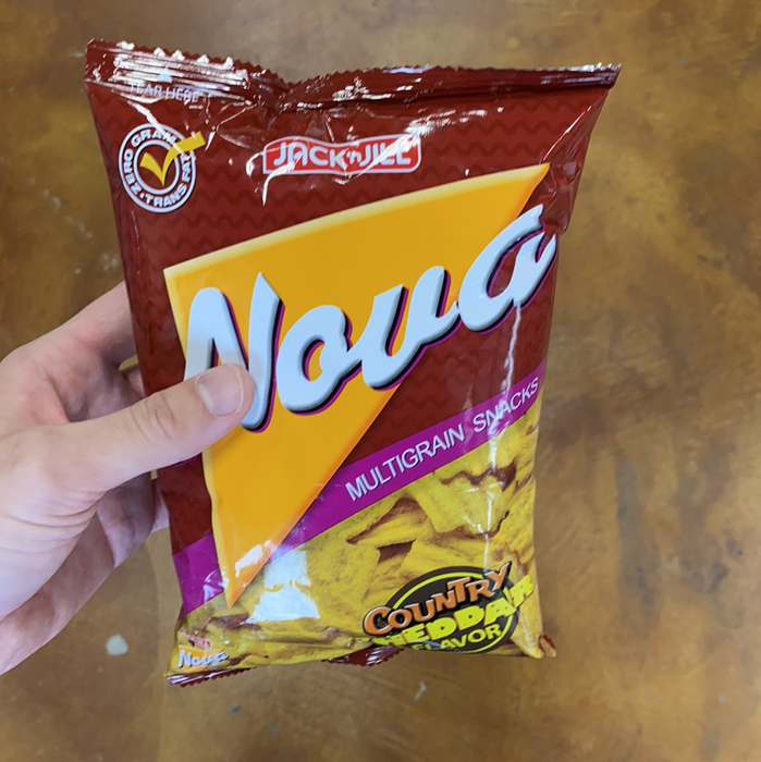 A hand holding a bag of Jack ‘n Jill Nova Country Cheddar flavored multigrain snacks