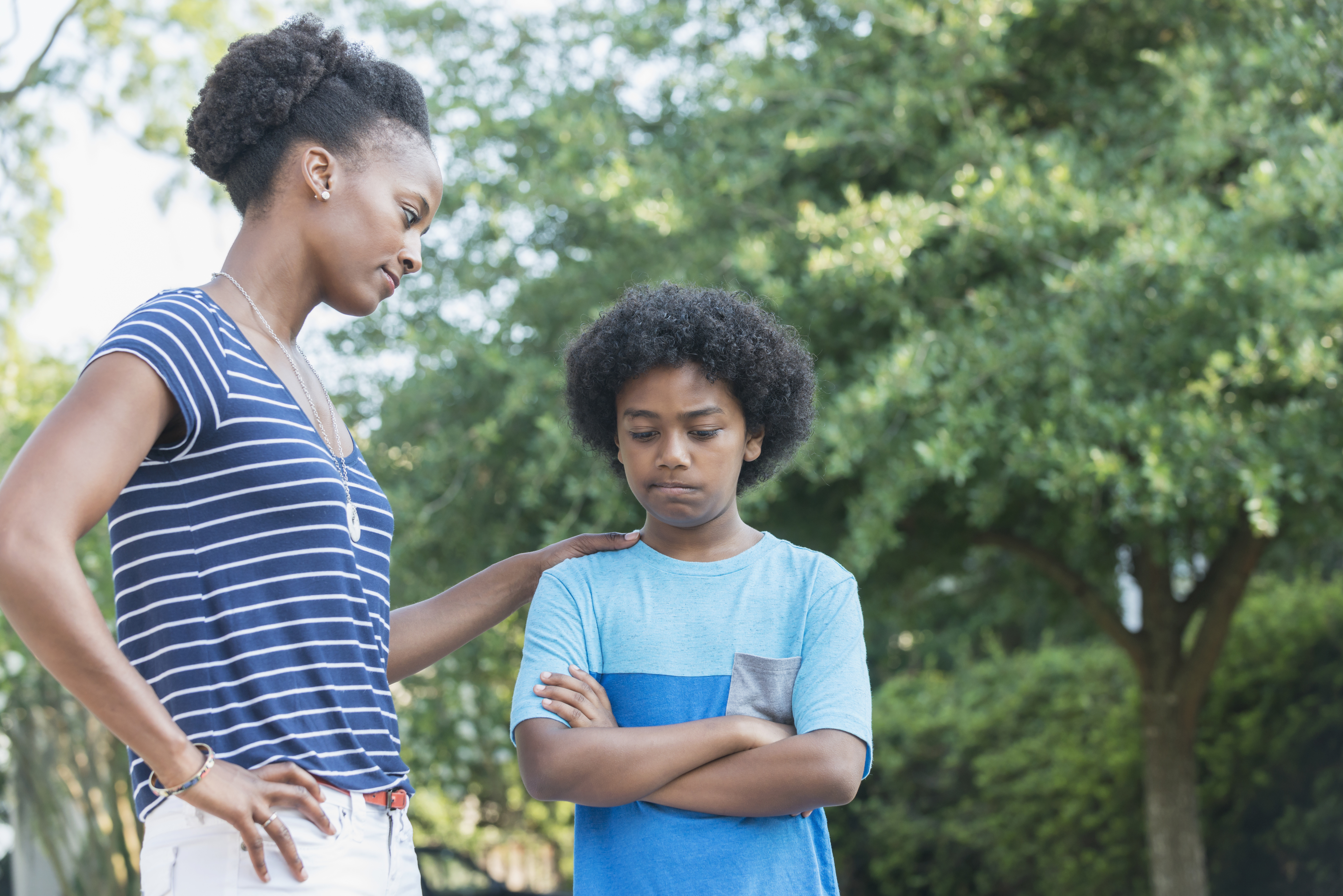 Mother and son talking outside, with the mother placing her hand on the boy's shoulder. The boy has his arms crossed, looking down