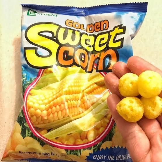 A hand holding five corn puffs in front of a bag labeled &quot;Golden Sweet Corn&quot; with an image of corn on the cob