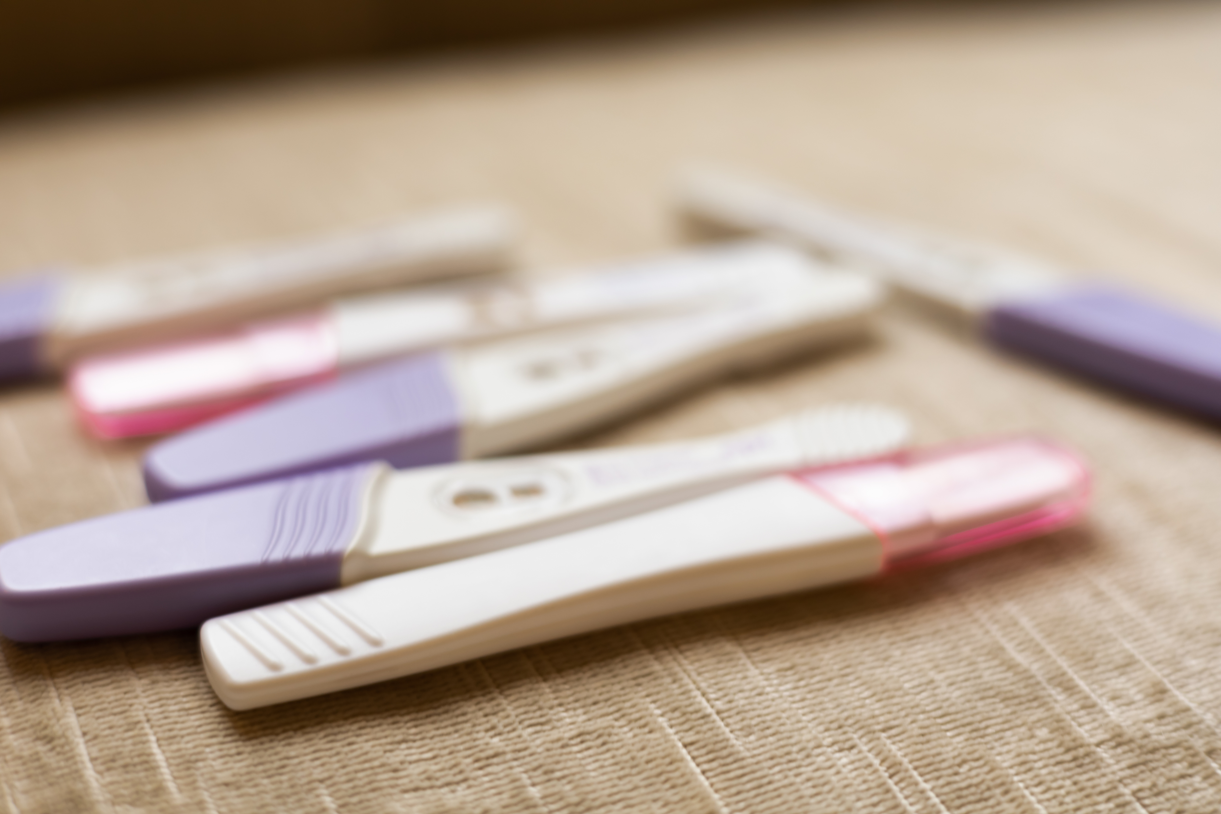 Several home pregnancy tests with various results arranged on a beige surface