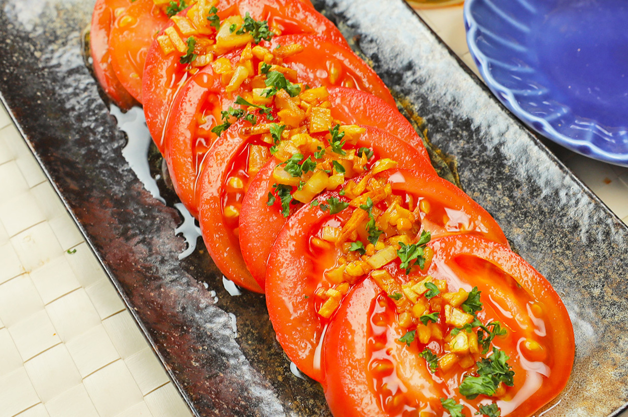 トマトのスライスがきれいに並べられ、上にみじん切りのハーブと調味料が乗っている前菜の写真。