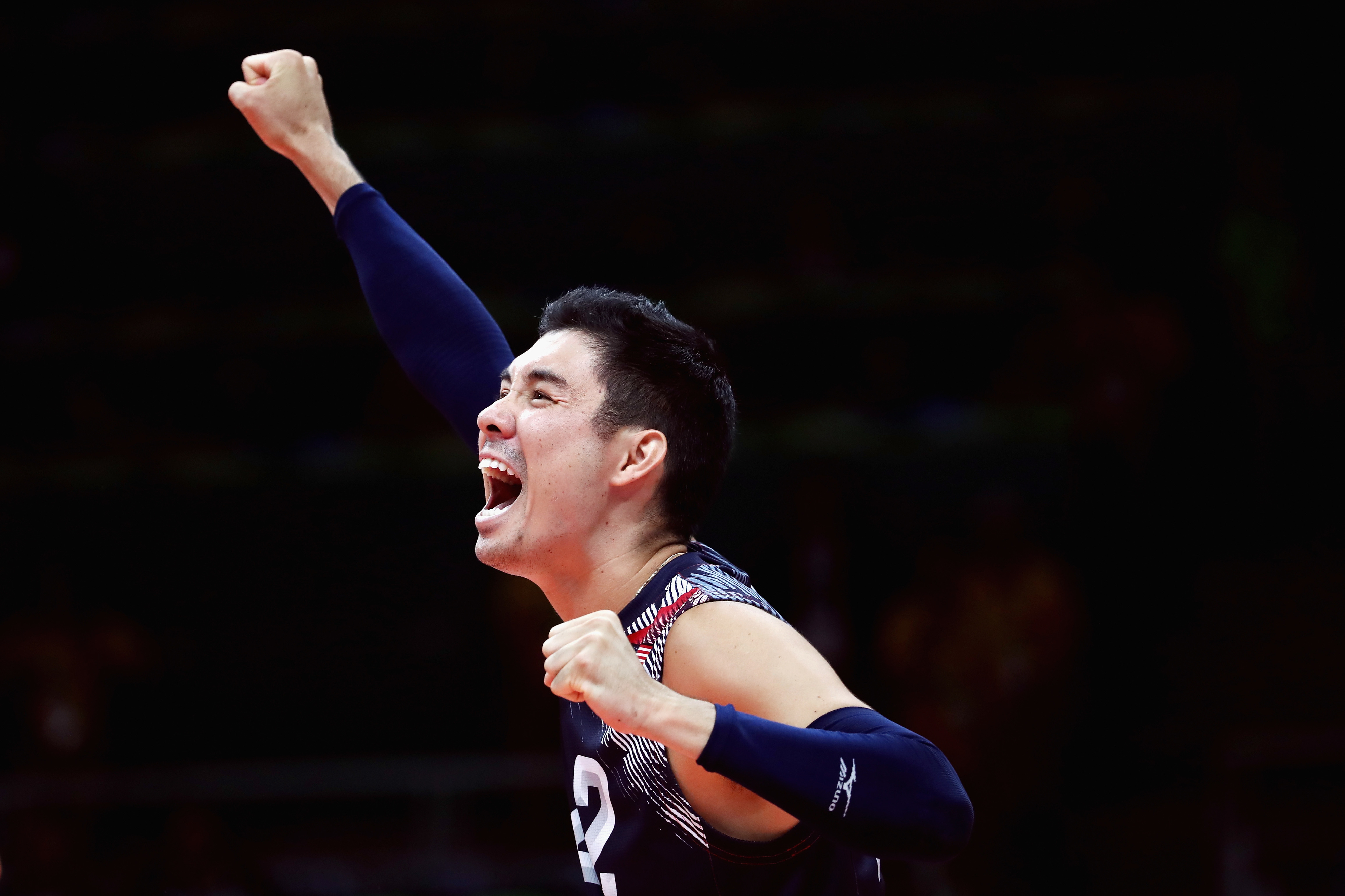 A volleyball player in a jersey with the number 12 is cheering with a fist raised during a match