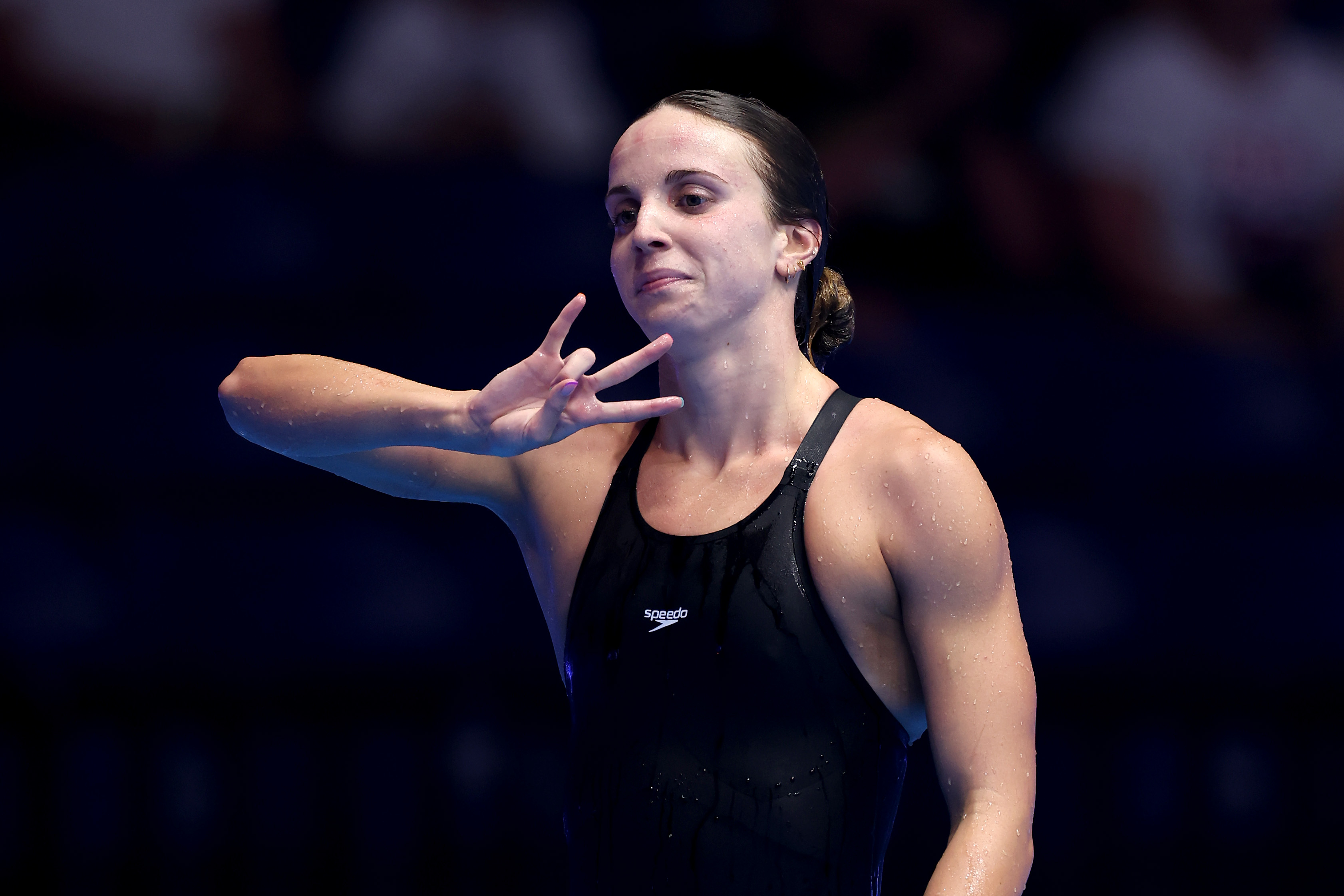 Female swimmer in a black swimsuit making a hand gesture on the poolside after a competition