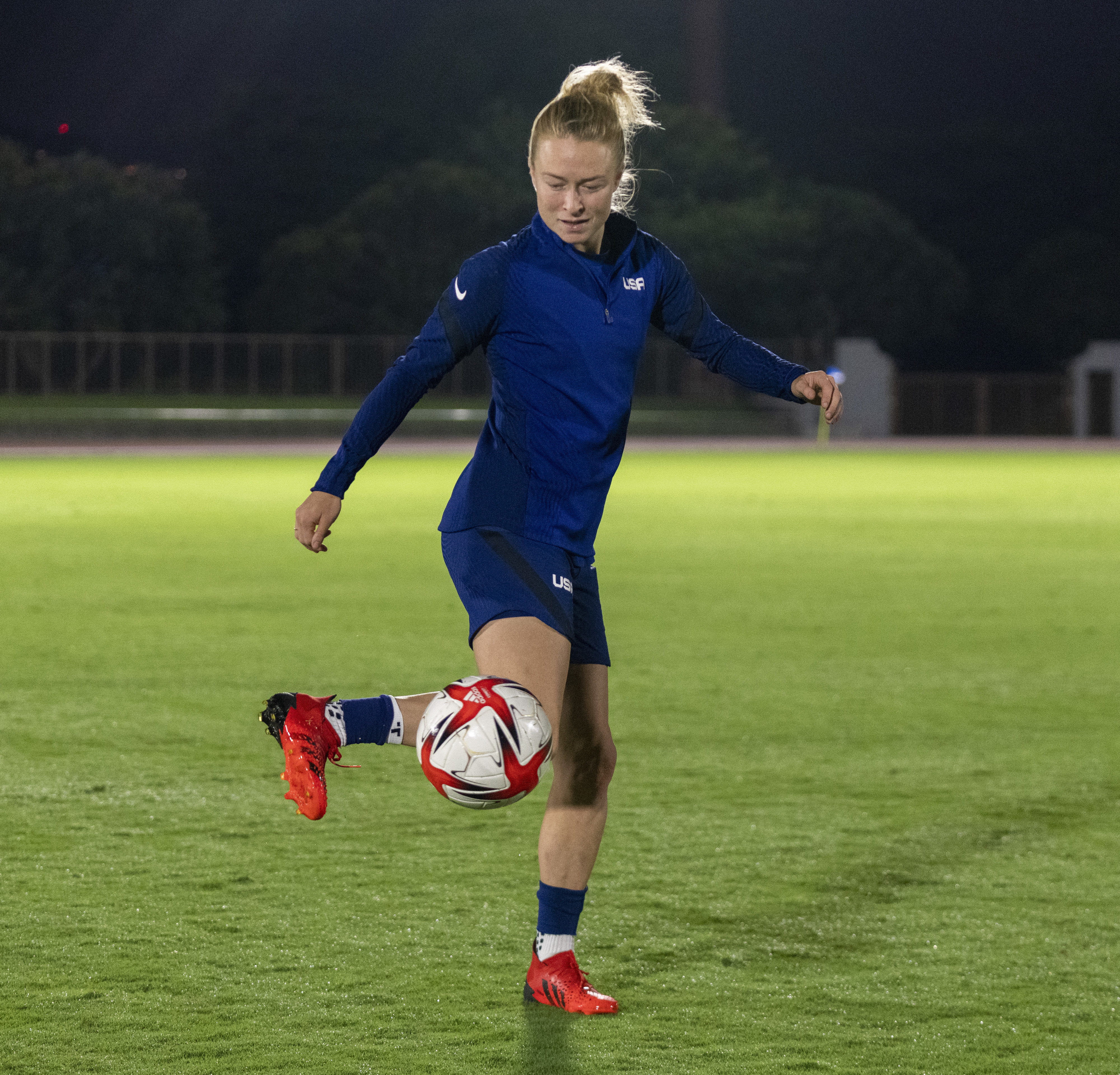 USA player balances a soccer ball during practice on a field at night