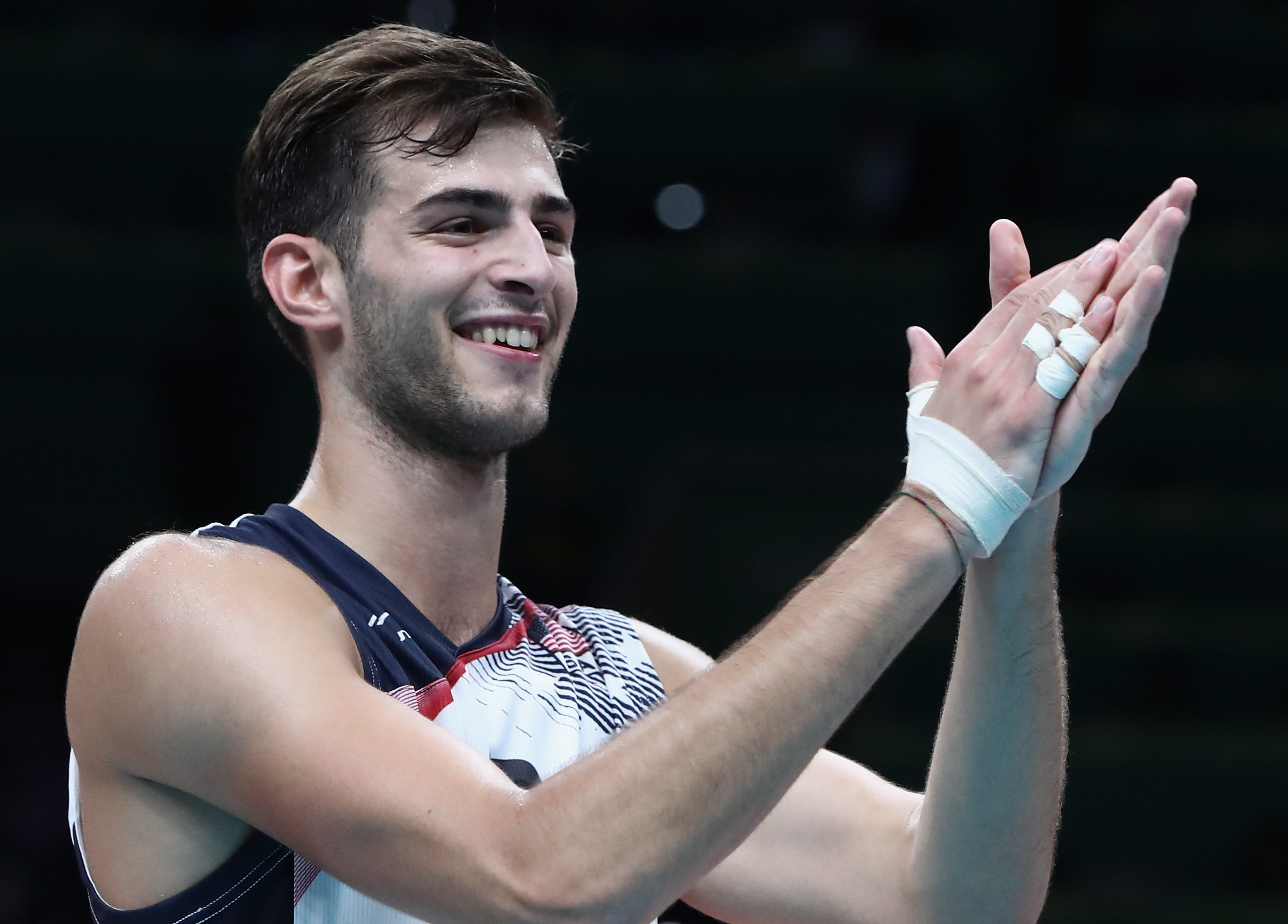Volleyball player clapping with a smile after a match, wearing a sleeveless sports jersey, with fingers taped for support