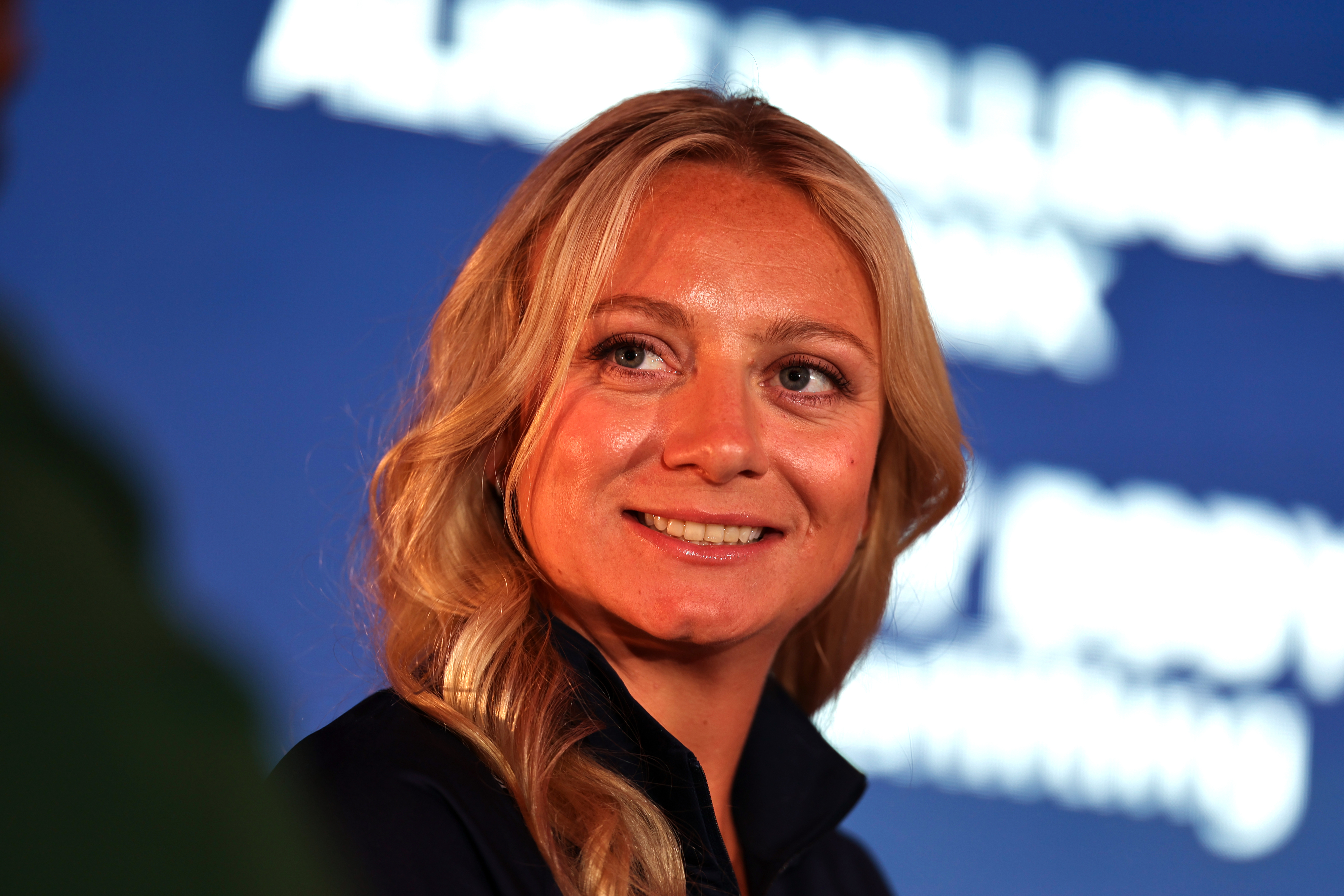 Woman with long blonde hair smiles in a sports event background