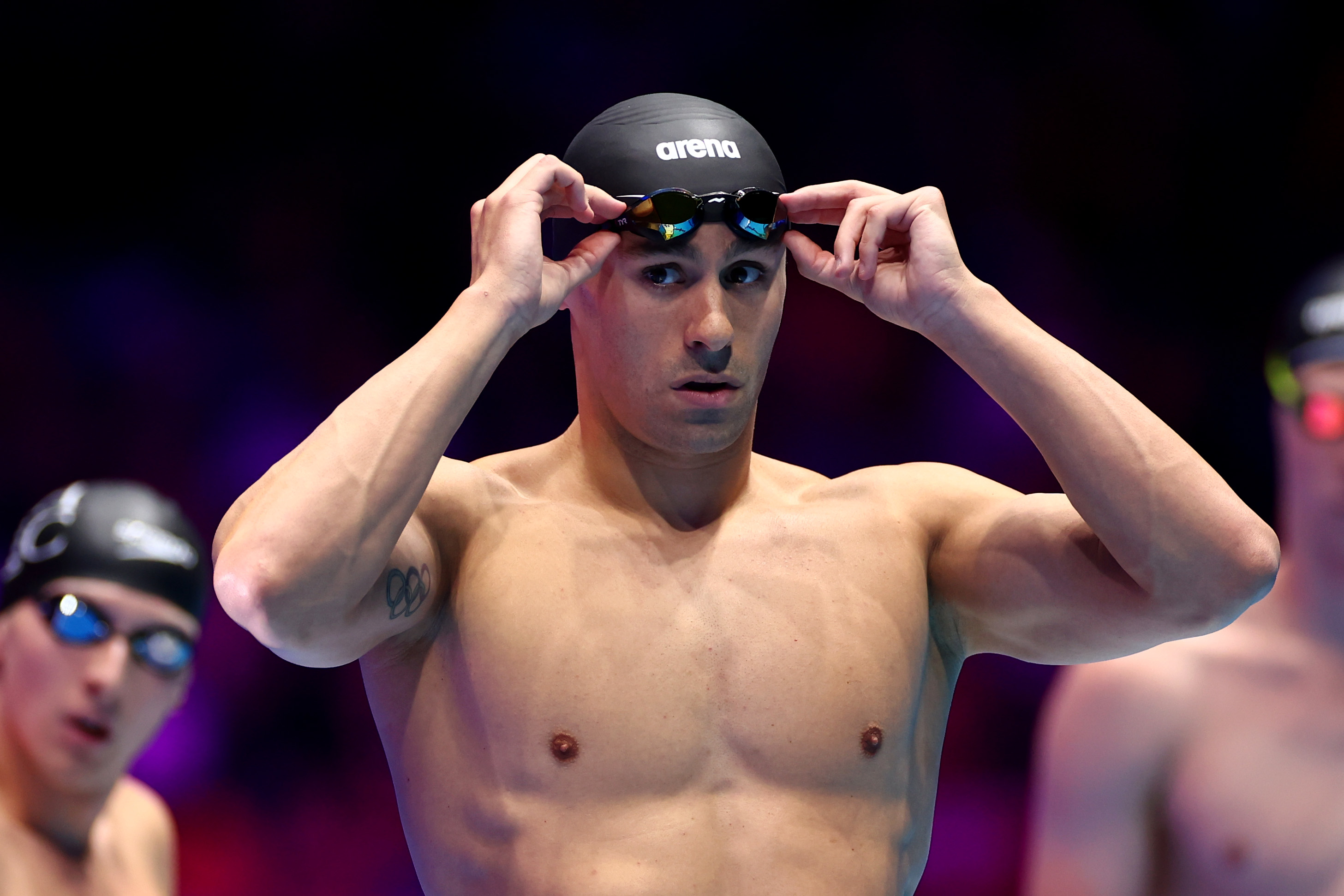 Olympic swimmer adjusts his goggles before a race. Other swimmers in the background prepare as well