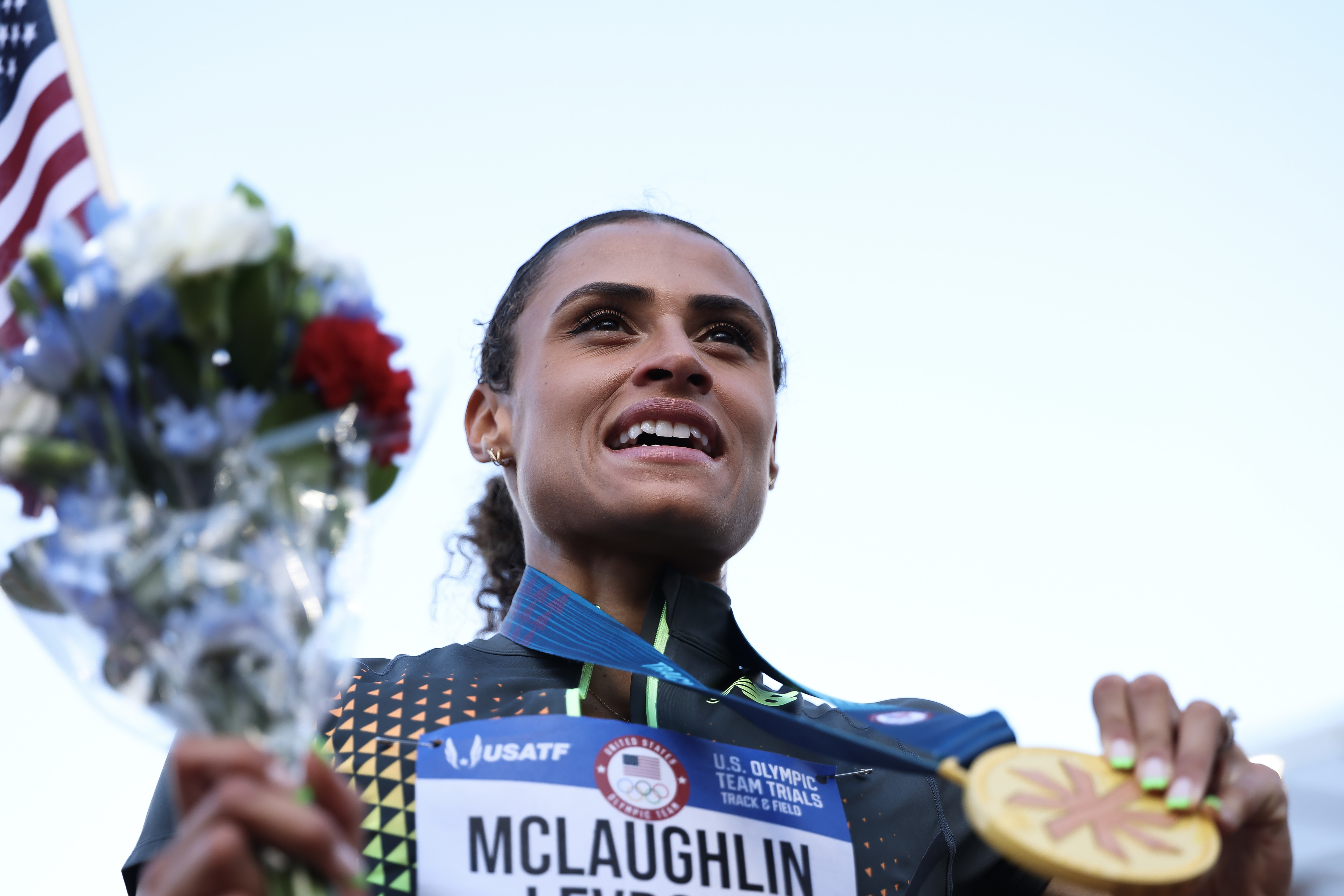 Sydney McLaughlin holds a bouquet and her gold medal after winning at the U.S. Olympic Team Trials. She wears her racing uniform and a name bib
