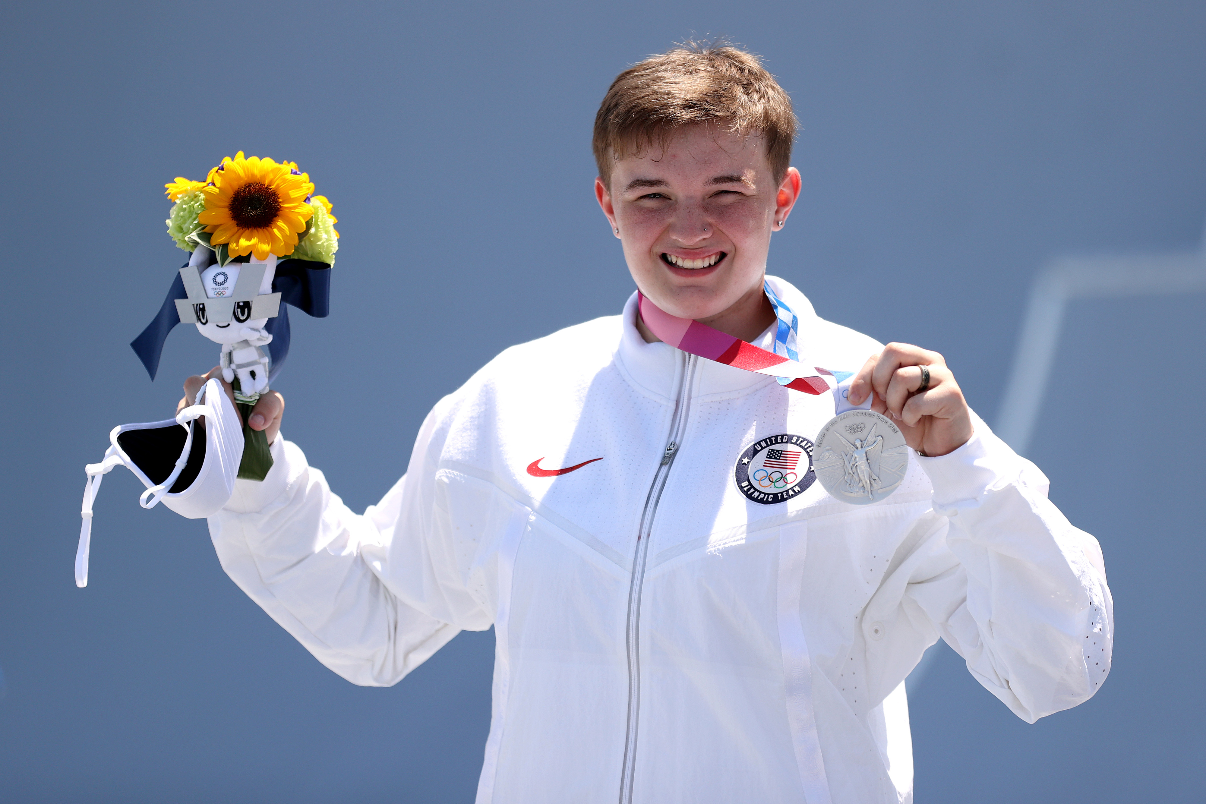 Hannah Roberts celebrates holding silver medal, bouquet of sunflowers, and mascot plush toy