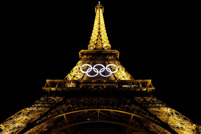 The Eiffel Tower illuminated at night with the Olympic rings displayed, promoting the upcoming Paris Olympic Games