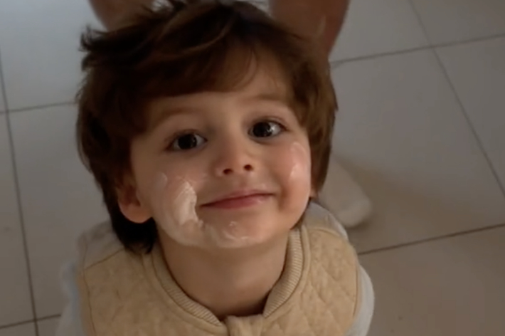 幼い男の子が顔にクリームを塗ったままカメラを見上げています。