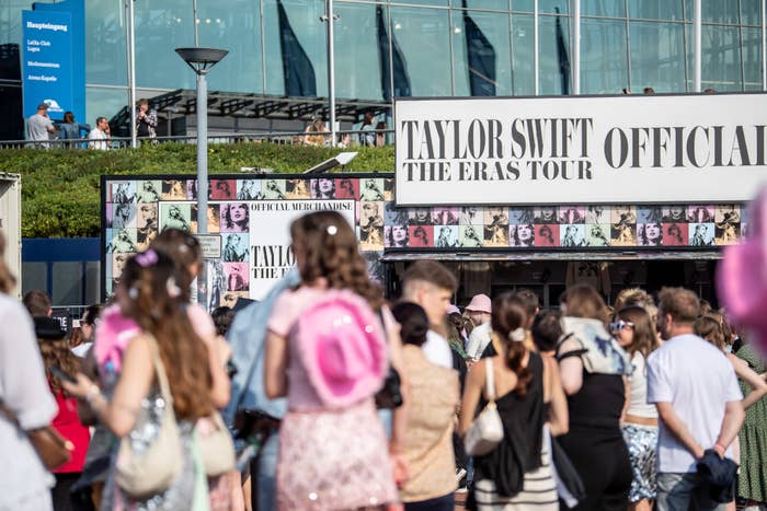 Crowd gathered outside a building with a sign for "Taylor Swift The Eras Tour Official Merchandise."