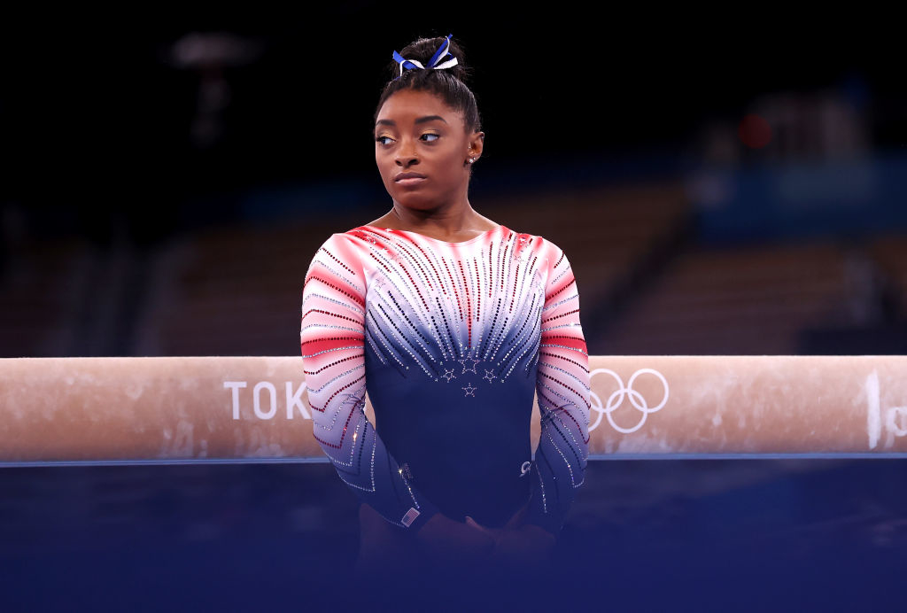 Simone Biles wearing a sparkling leotard, standing in front of a balance beam at the Tokyo Olympics