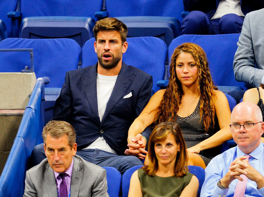 Gerard Piqué and Shakira sitting closely together at an event, holding hands, with three other individuals seated in front of them