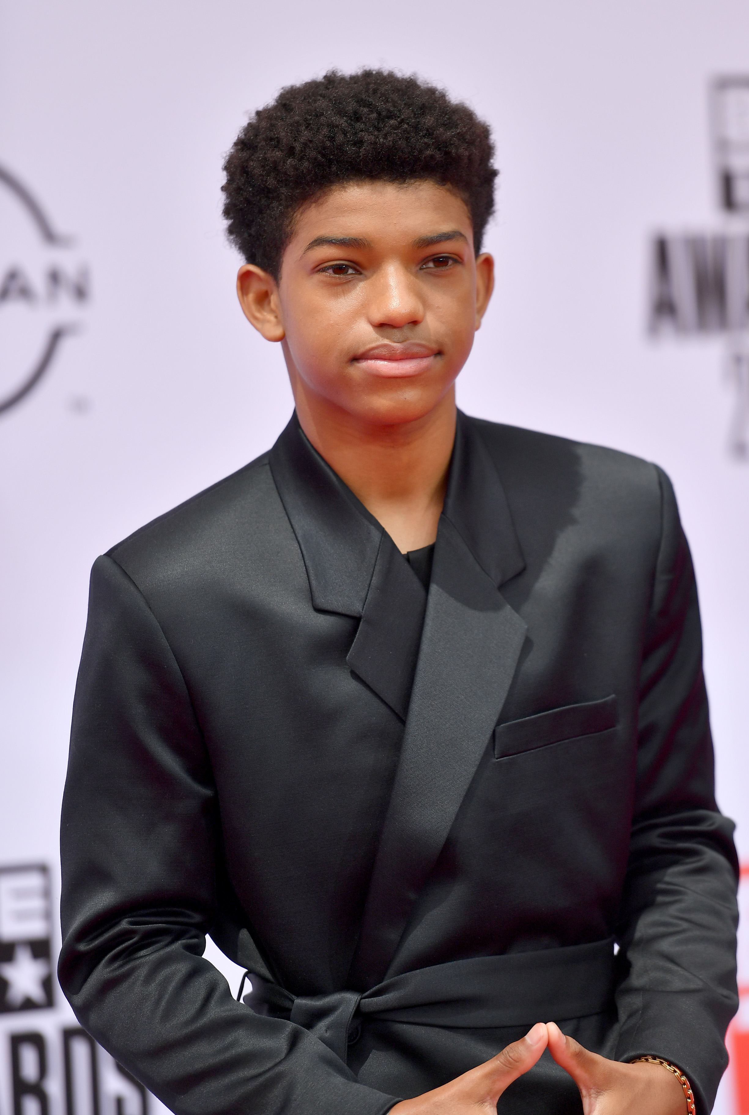 Young male celebrity wearing a stylish black suit jacket, posing for a photo on the red carpet at an event