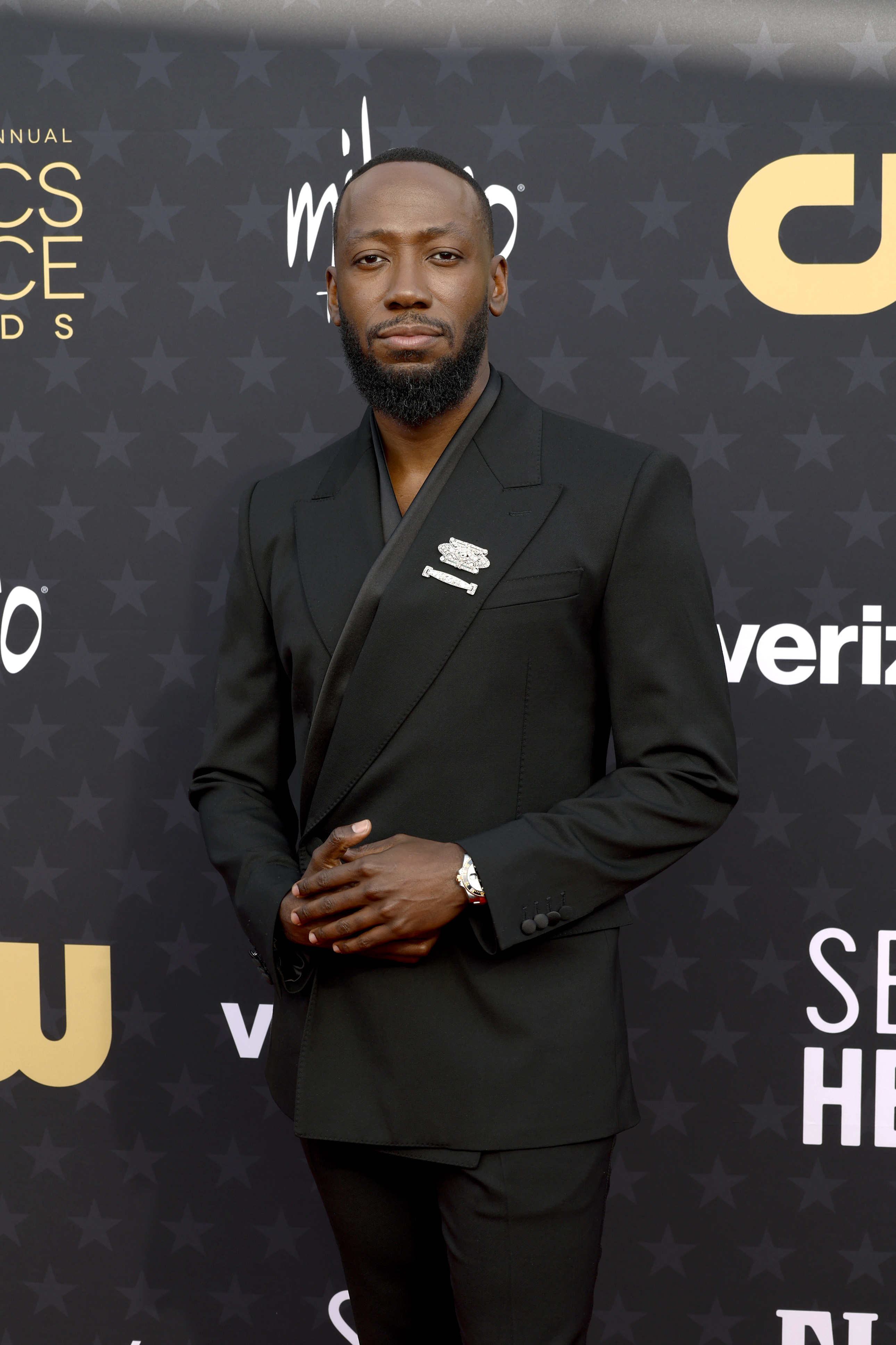 Lamorne Morris in a black double-breasted suit at an event with logos in the background