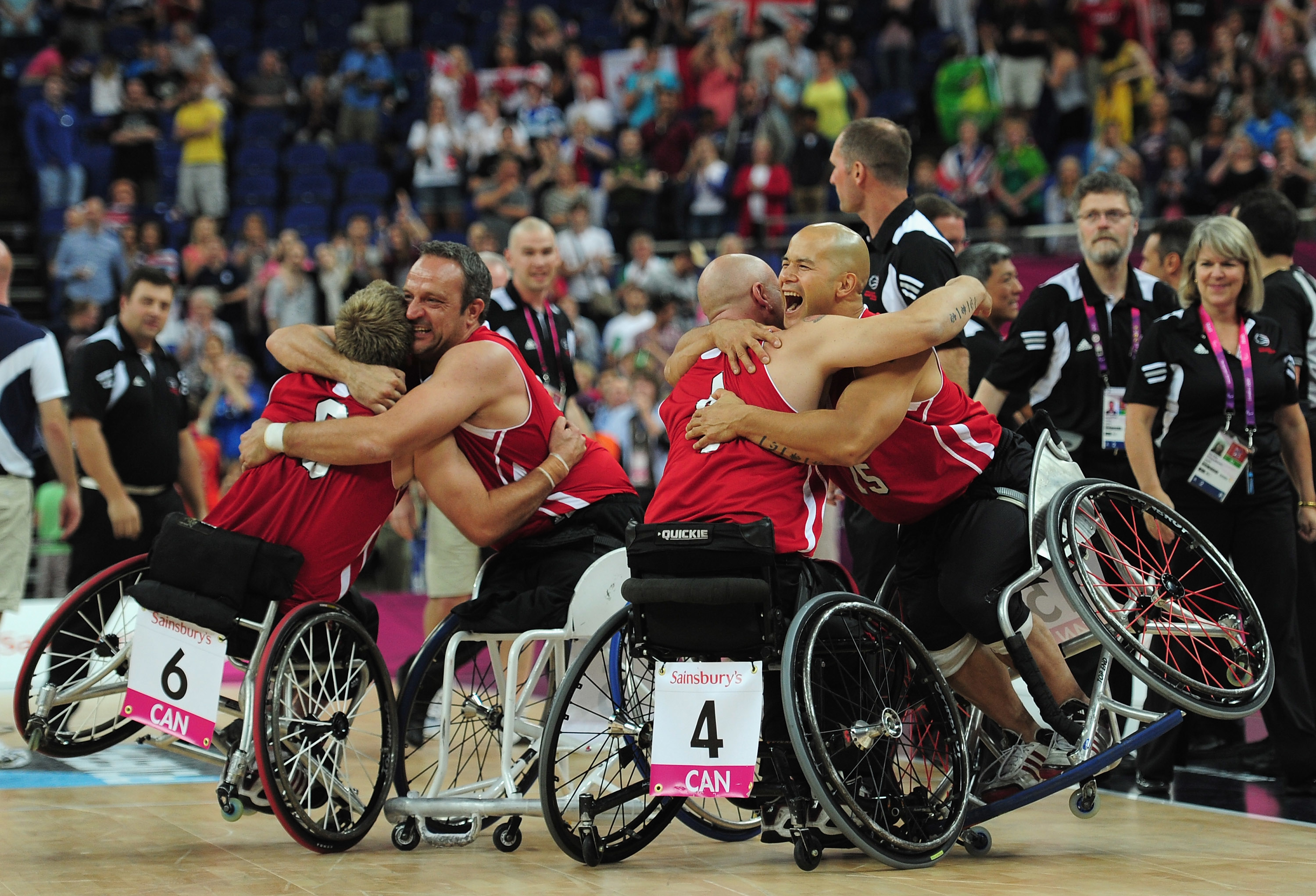 Team Canada wheelchair rugby players, identifiable by their jerseys numbered 6 and 4, celebrating during a match, surrounded by a cheering crowd