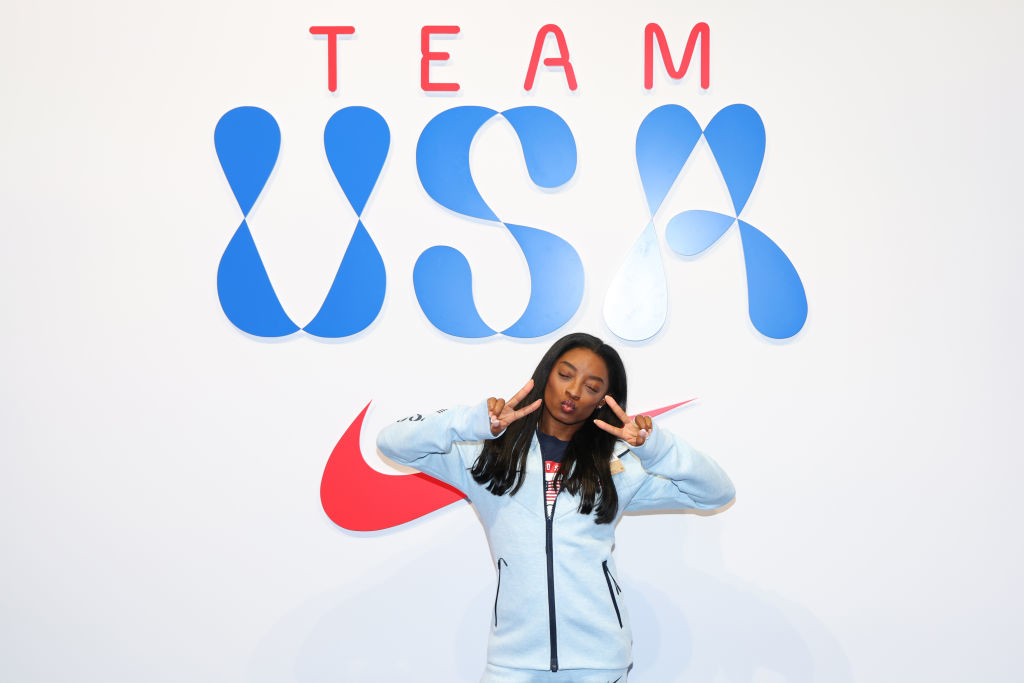 Simone Biles poses with peace signs in front of a &quot;Team USA&quot; sign at a promotional event