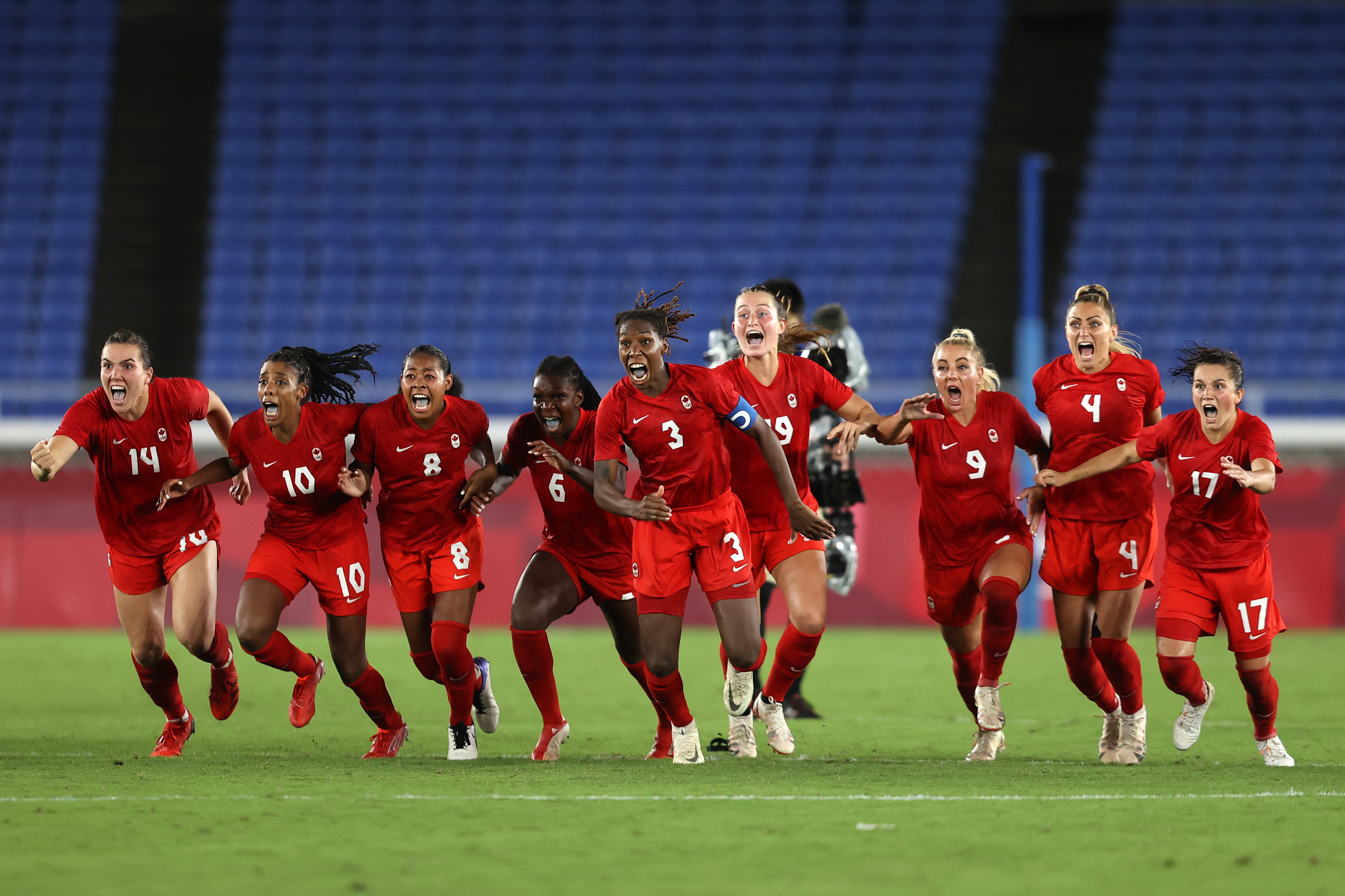 A group of female soccer players, wearing matching team uniforms, celebrate on the field. Several players are mid-motion, expressing joy and excitement