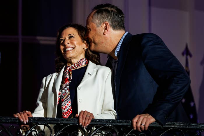 Kamala Harris, in a white blazer and patterned scarf, and Doug Emhoff, in a dark suit, share a warm moment on a balcony