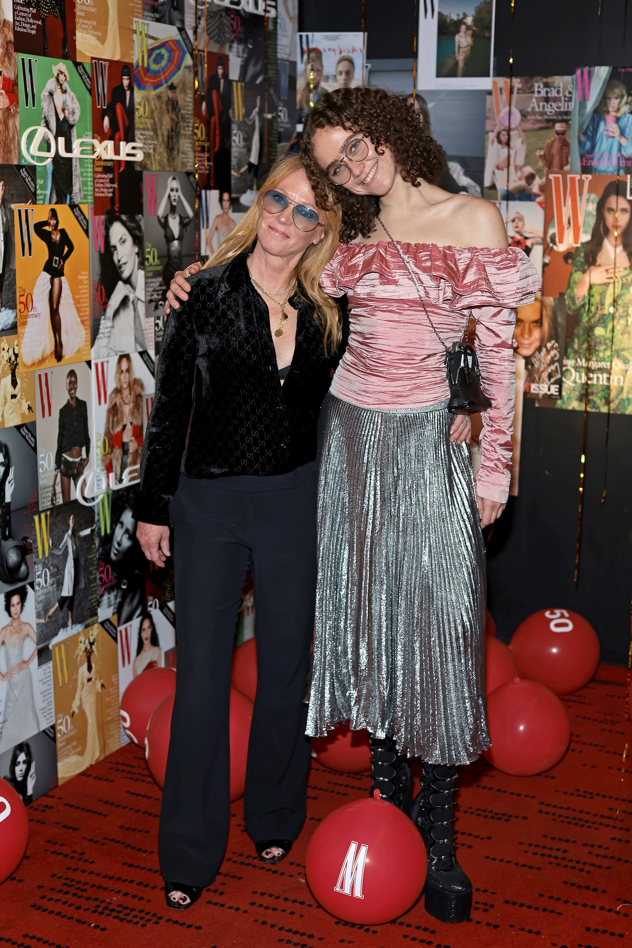 Kerstin and Ella Emhoff pose on the red carpet; Uma wears a black outfit, Maya wears an off-shoulder top with a metallic skirt and platform boots