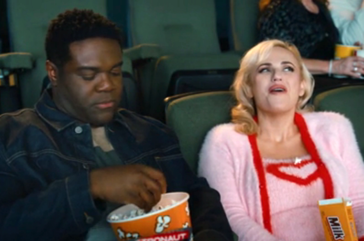 Sam Richardson and Rebel Wilson sit next to each other in a movie theater, holding popcorn and Milk Duds, as Seth and Stephanie in Senior Year
