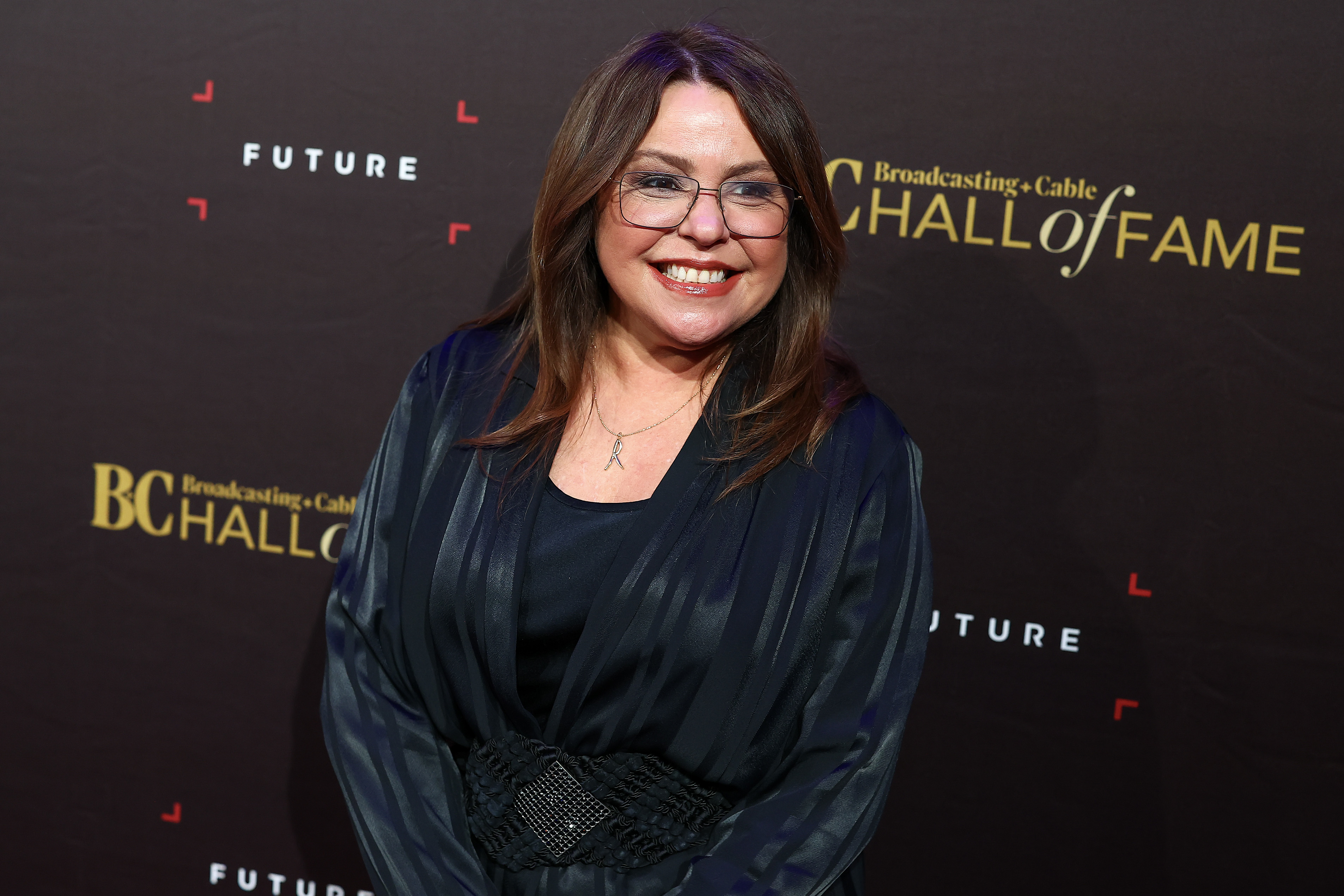 Rachael Ray at the Broadcasting & Cable Hall of Fame event, wearing a black dress with a wide belt and glasses, posing on the red carpet