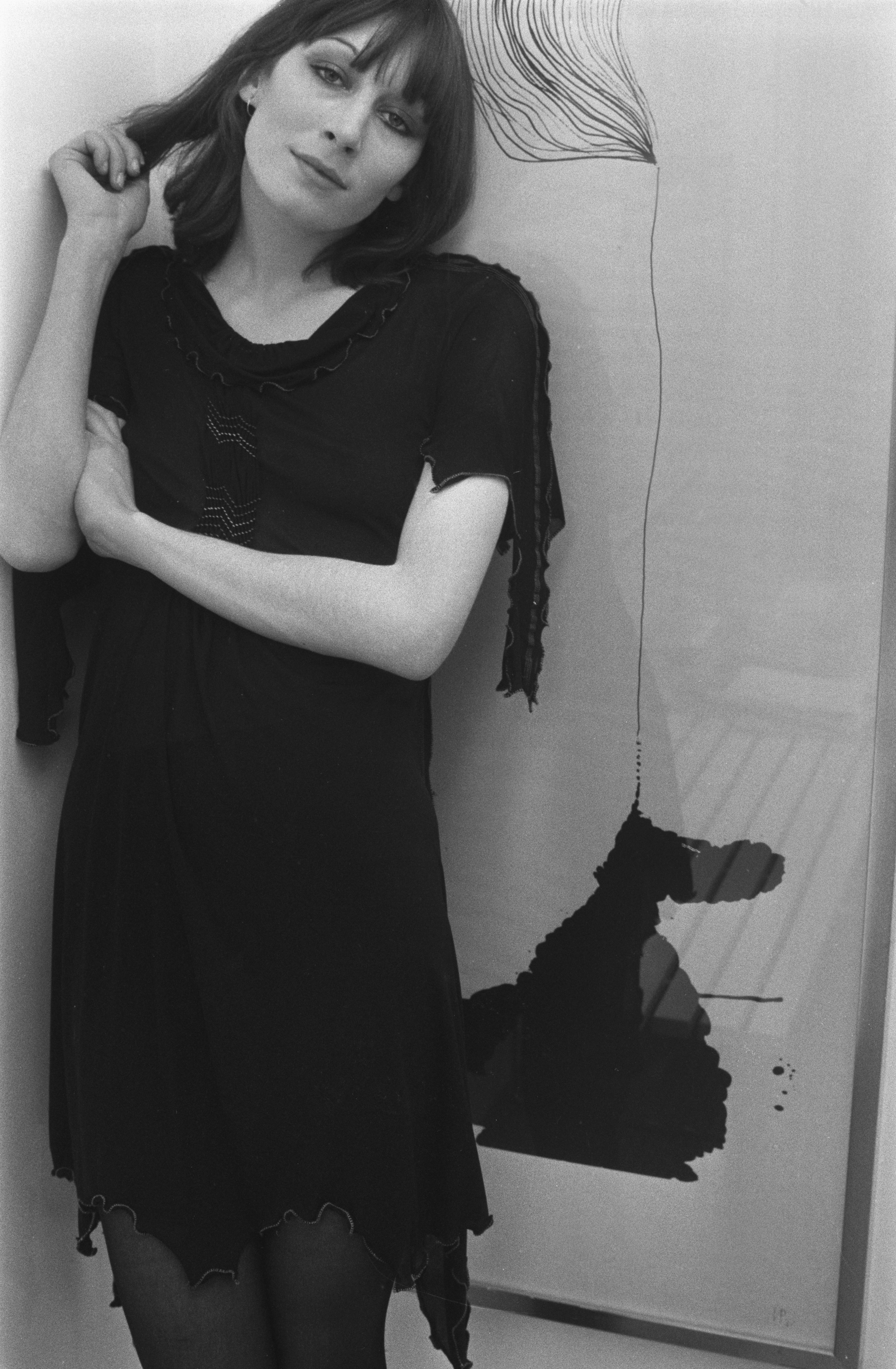 Anjelica Huston poses in a black dress against an abstract art background