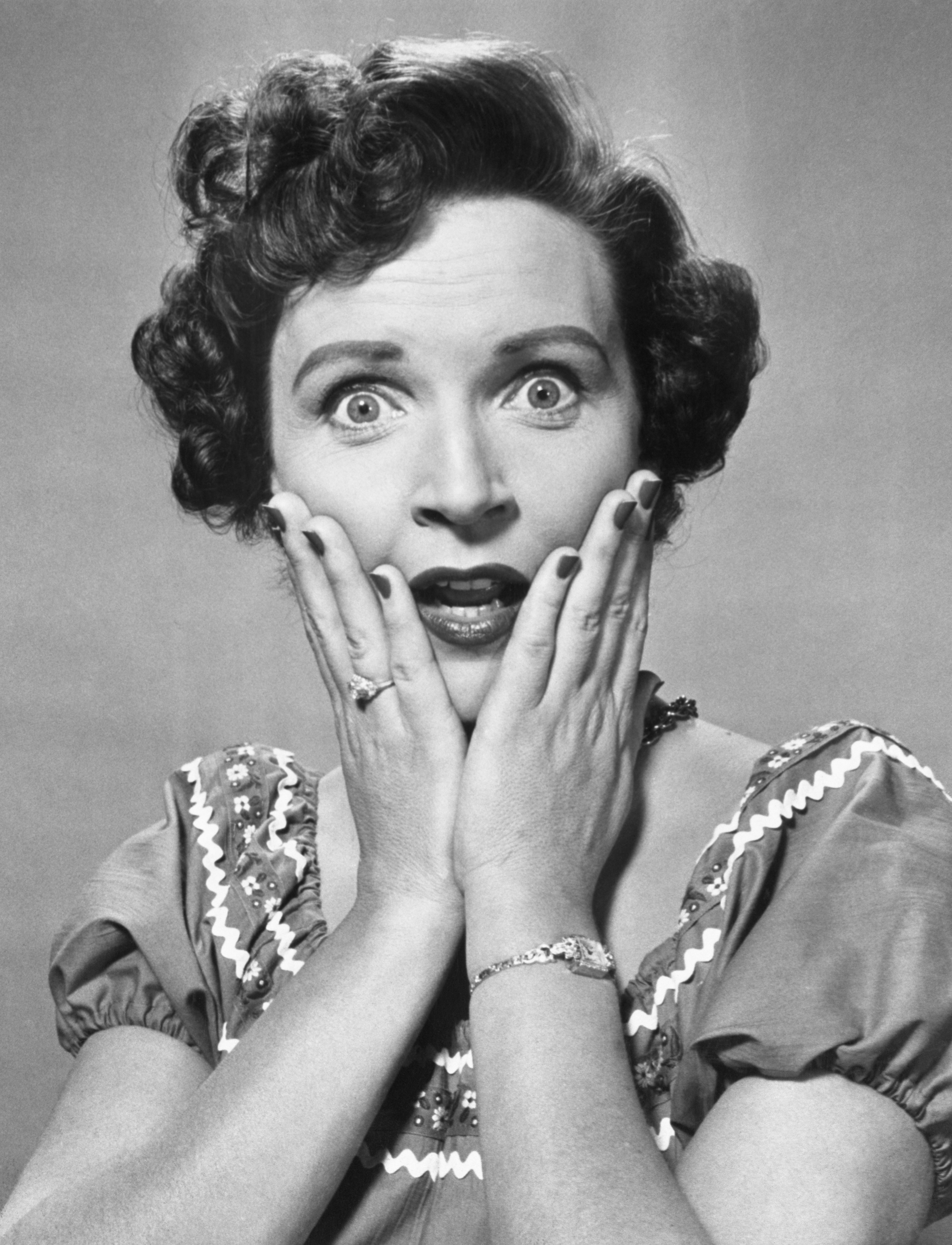 Betty White, eyes wide and hands on cheeks, wearing a short-sleeve dress in a classic retro style