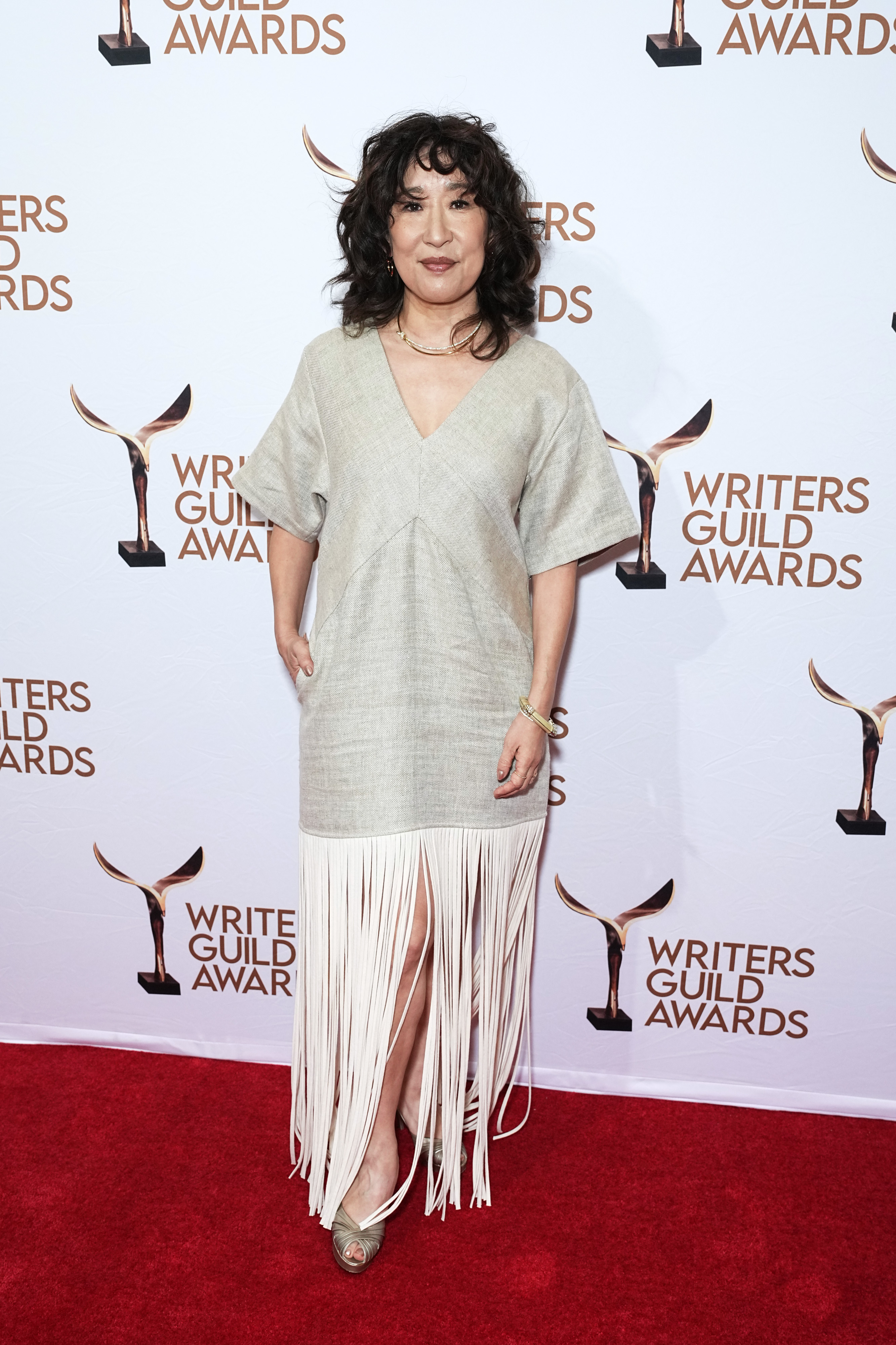 Sandra Oh on the red carpet at the Writers Guild Awards, wearing a light dress with a fringed hem