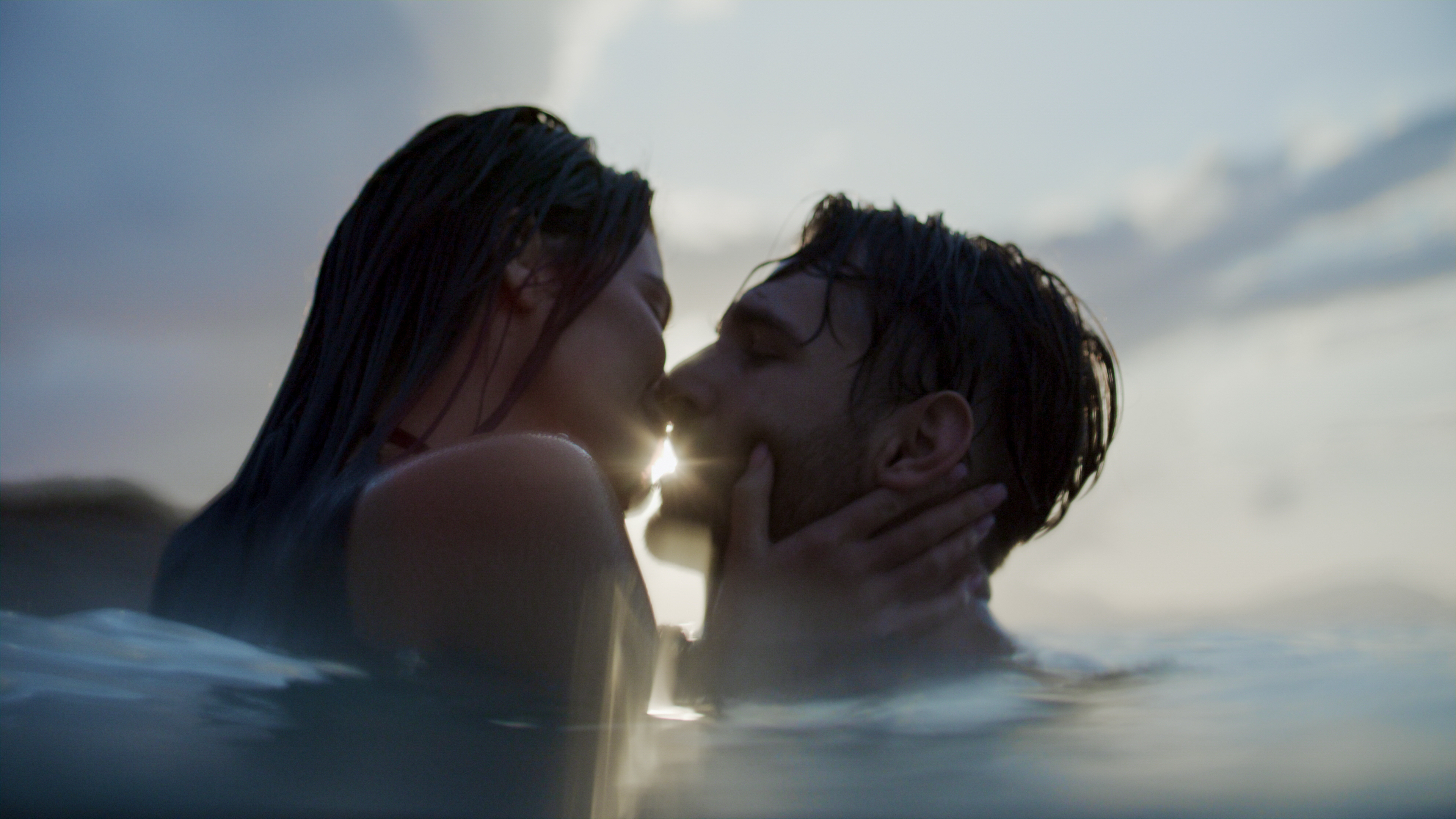 A couple shares a passionate kiss while partially submerged in water during sunset