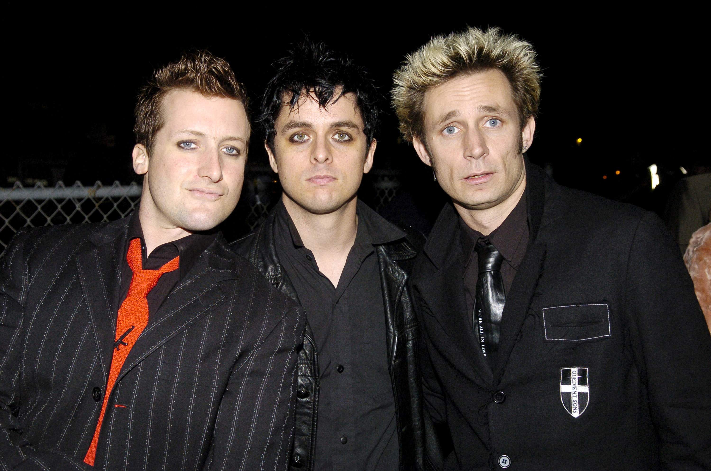 Tre Cool, Billie Joe Armstrong, and Mike Dirnt from the band Green Day wearing dark suits with bold ties, posing together at an event