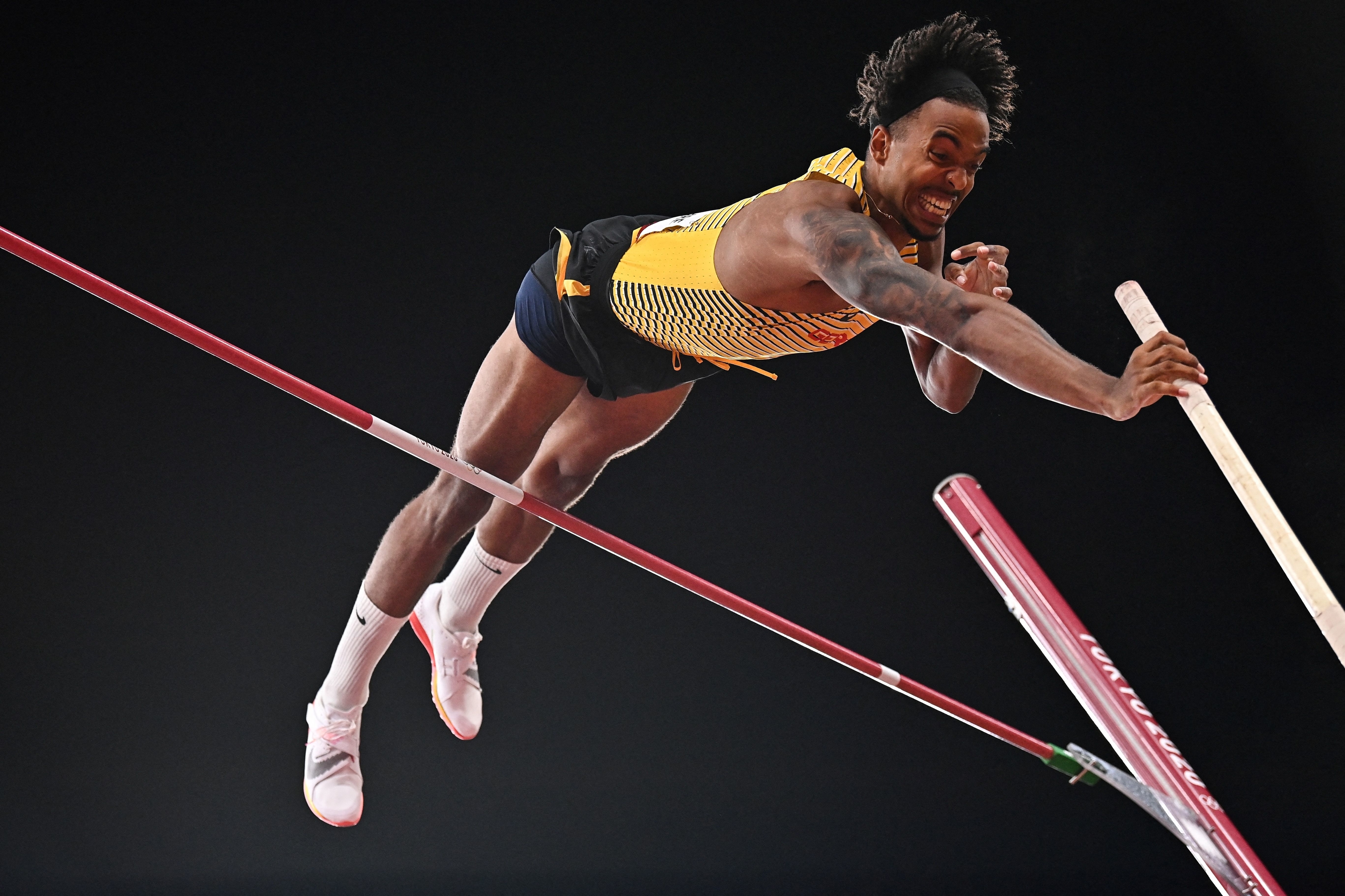 A pole vaulter successfully clears a high bar while holding a pole during an athletic event