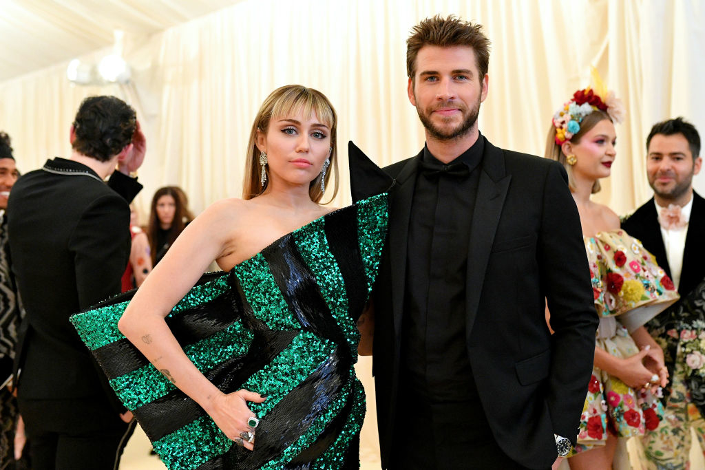 Miley Cyrus in a sequined geometric dress stands beside Liam Hemsworth in a tuxedo at a formal event