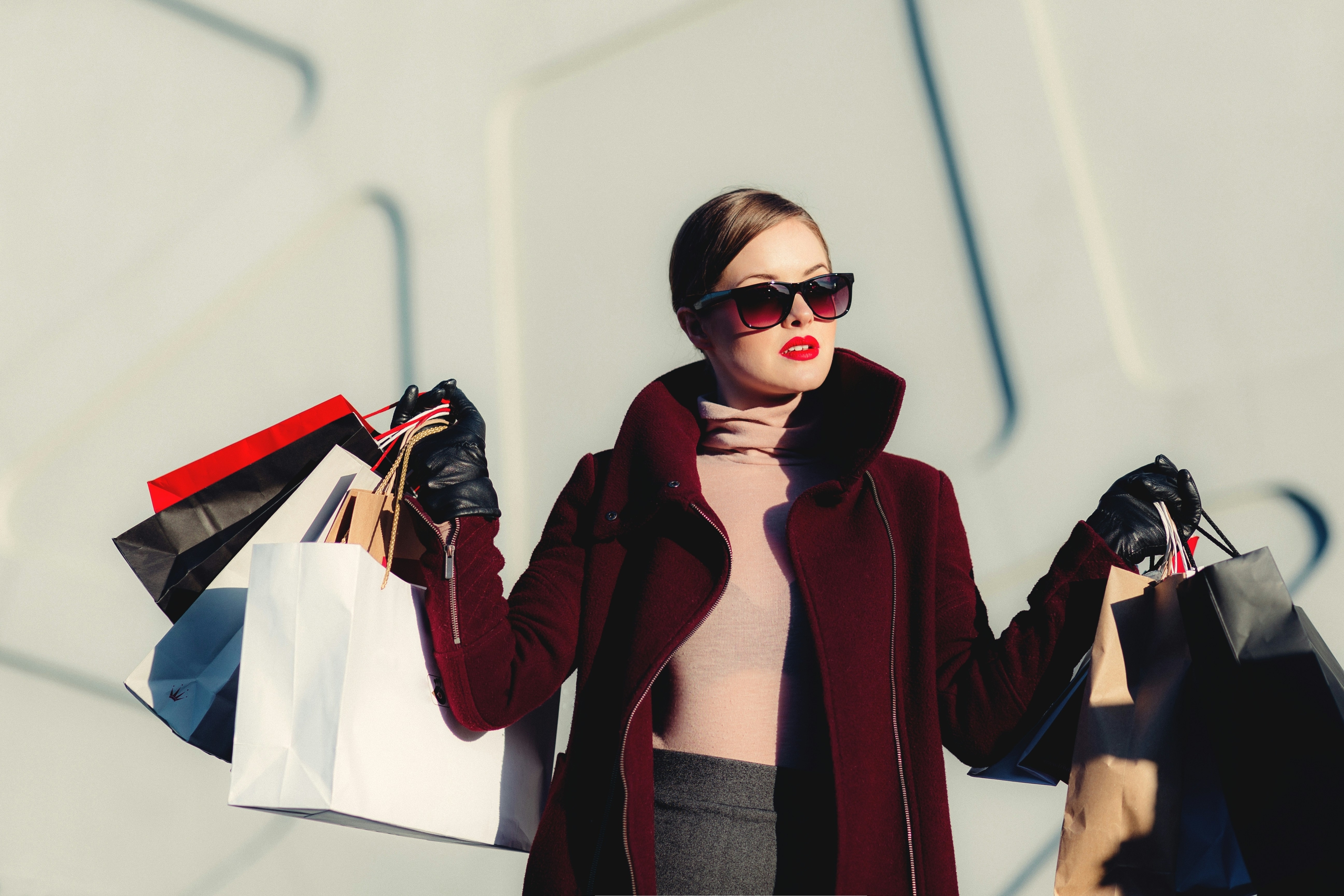 Woman in stylish winter coat holding multiple shopping bags with a confident expression, conveying a retail therapy theme