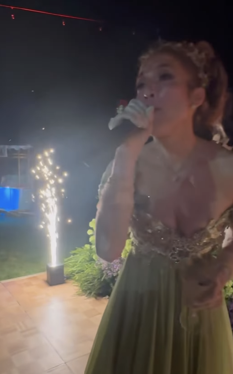 Jennifer speaking into a microphone with sparklers behind her
