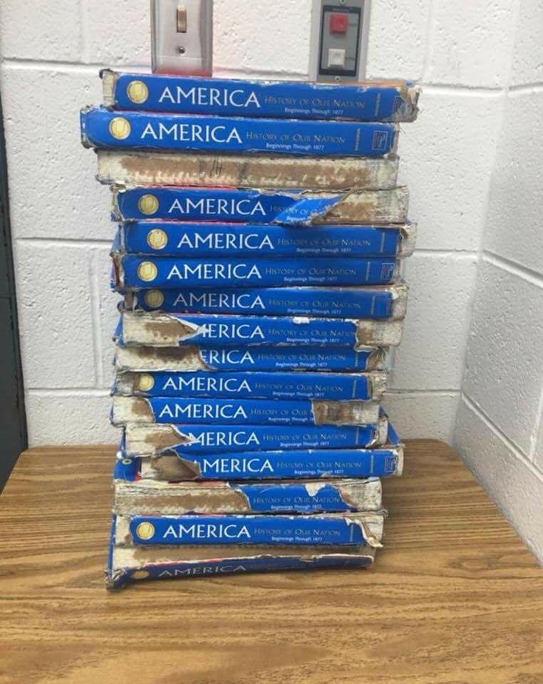 A stack of worn and damaged history textbooks titled "America: History of Our Nation" is piled on a table