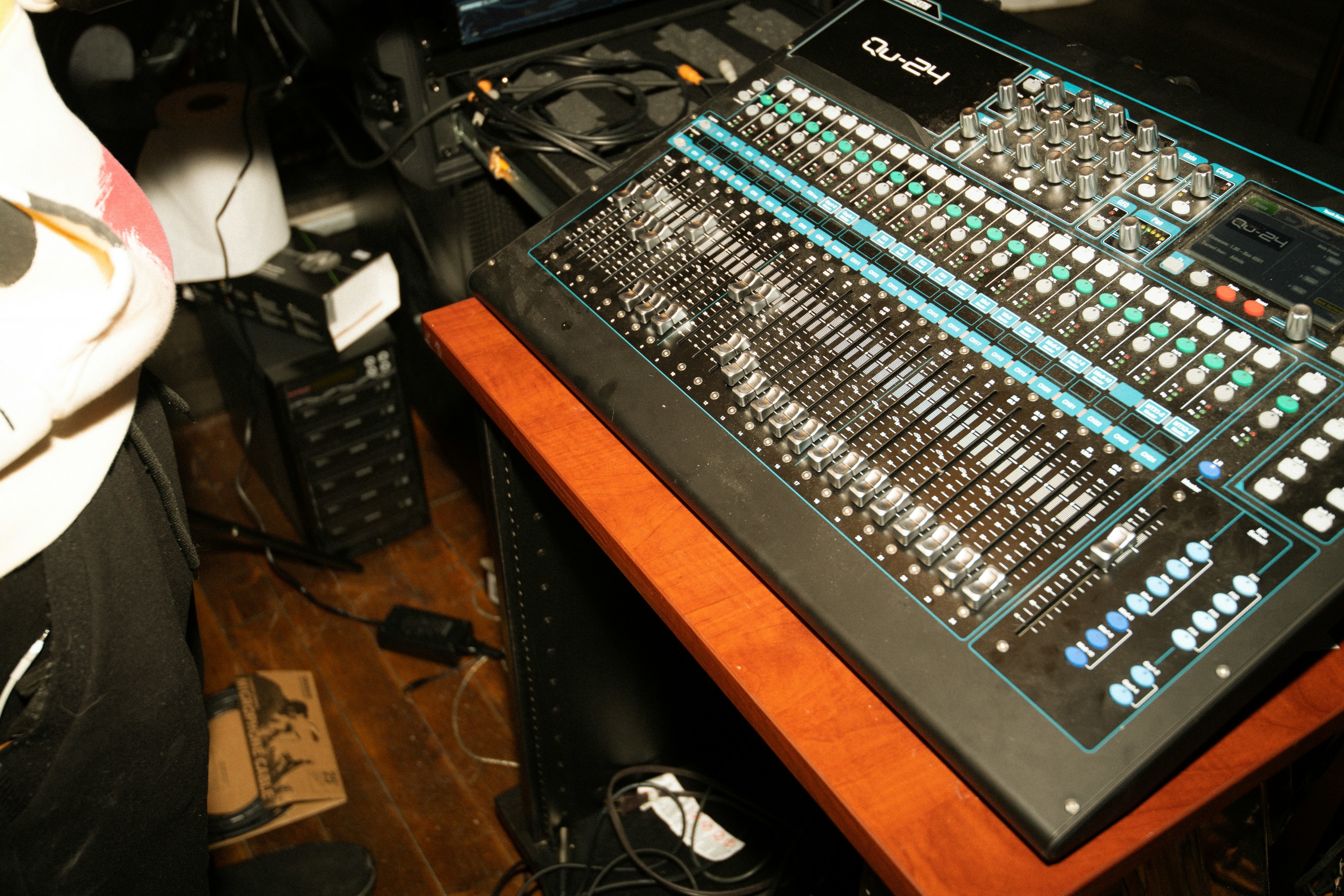 A close-up view of a sound mixing board on a wooden table, with various knobs, sliders, and buttons, in a recording studio setting