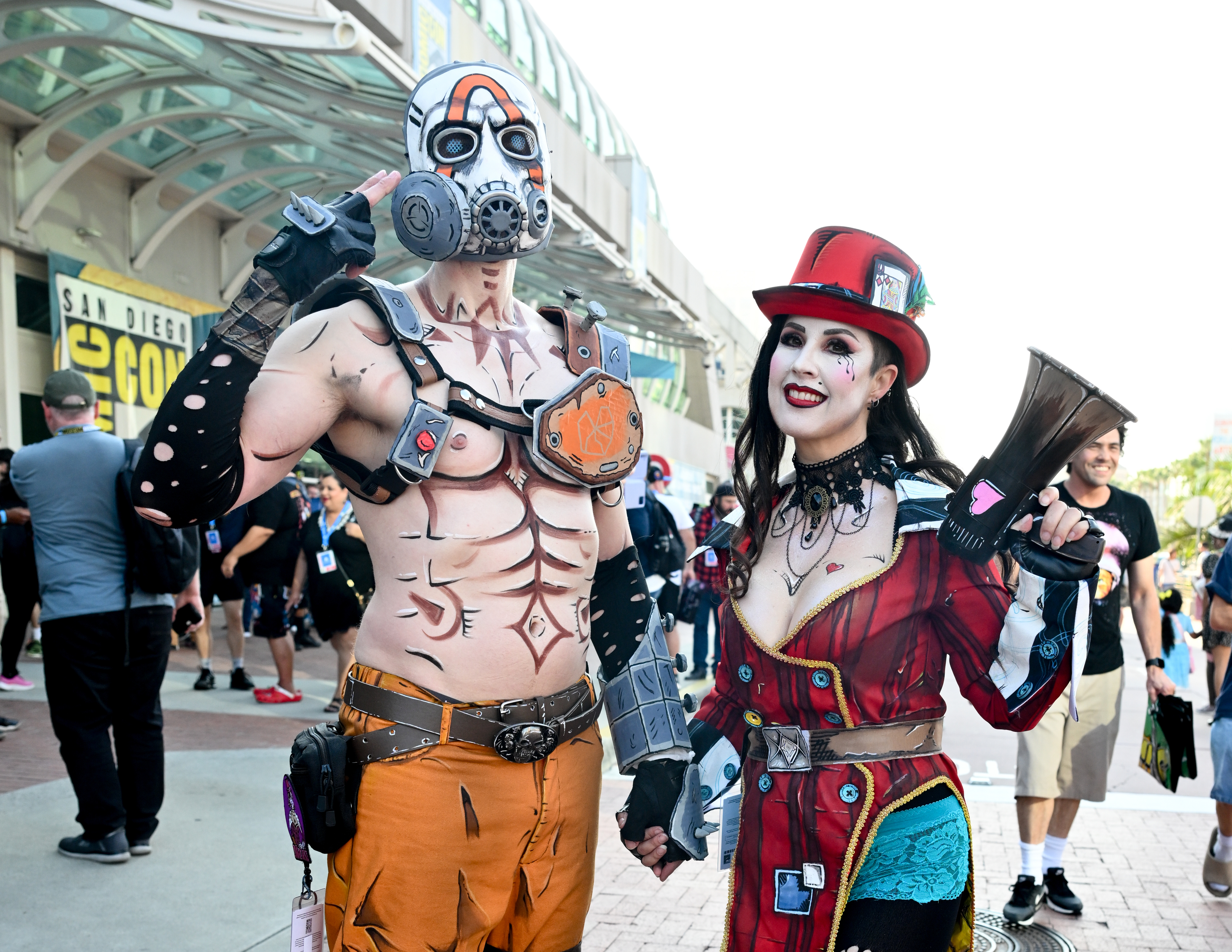 Individuals cosplaying as characters attend San Diego Comic-Con. One person wears a post-apocalyptic costume with a gas mask, and the other wears a steampunk-inspired outfit