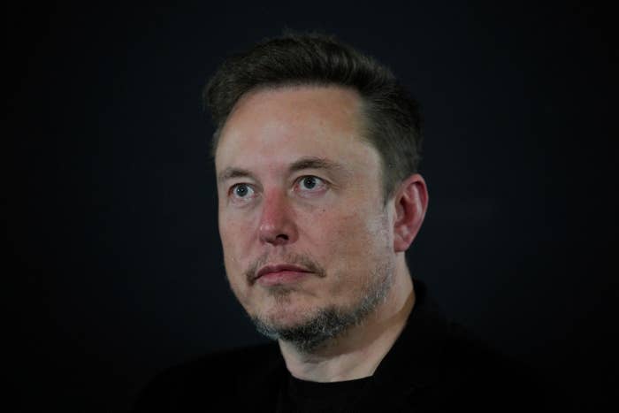 Elon Musk in a dark jacket, looking thoughtful against a dark background