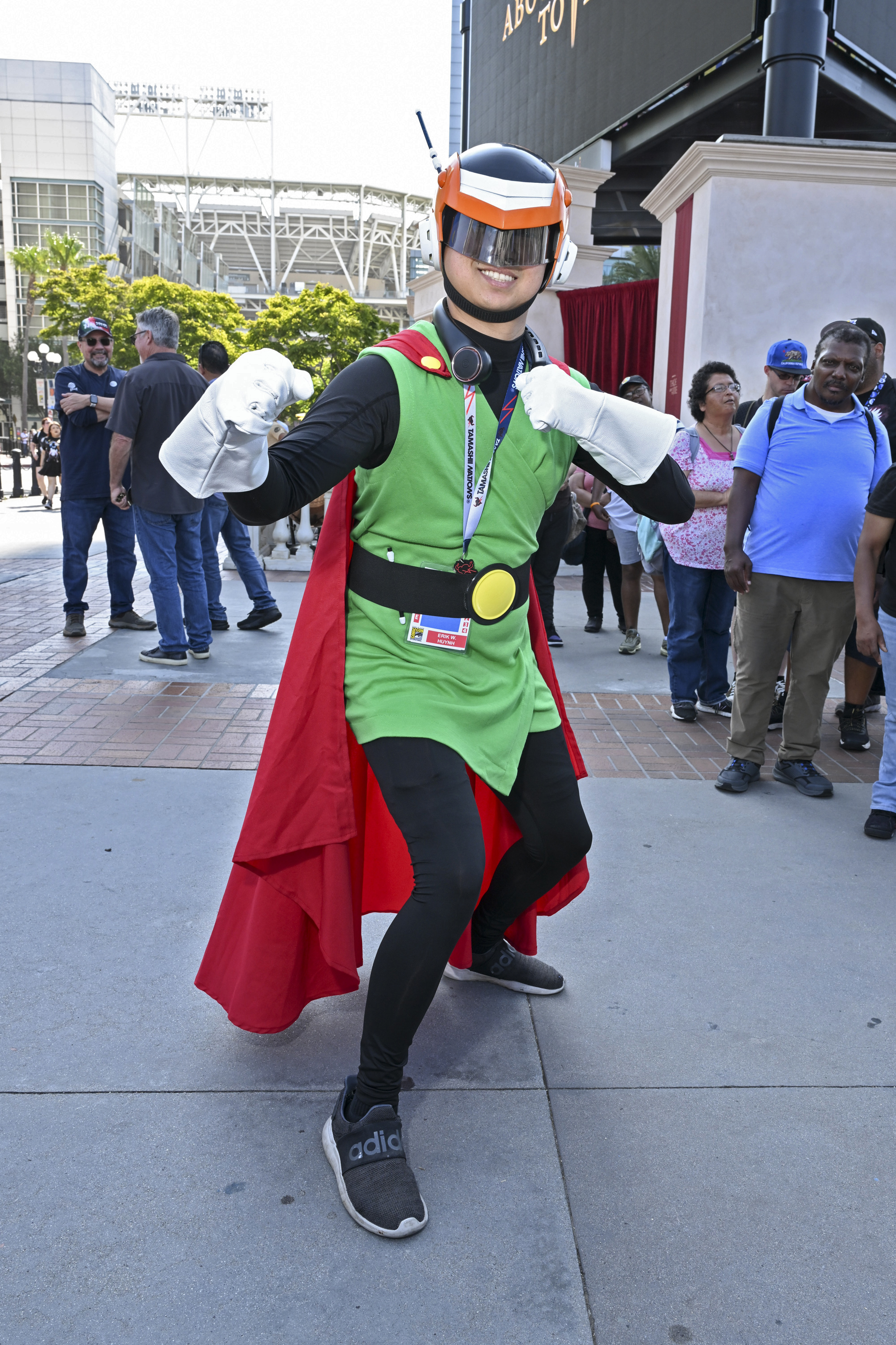 Person dressed as the Great Saiyaman from Dragon Ball Z striking a pose at an outdoor event with onlookers in the background