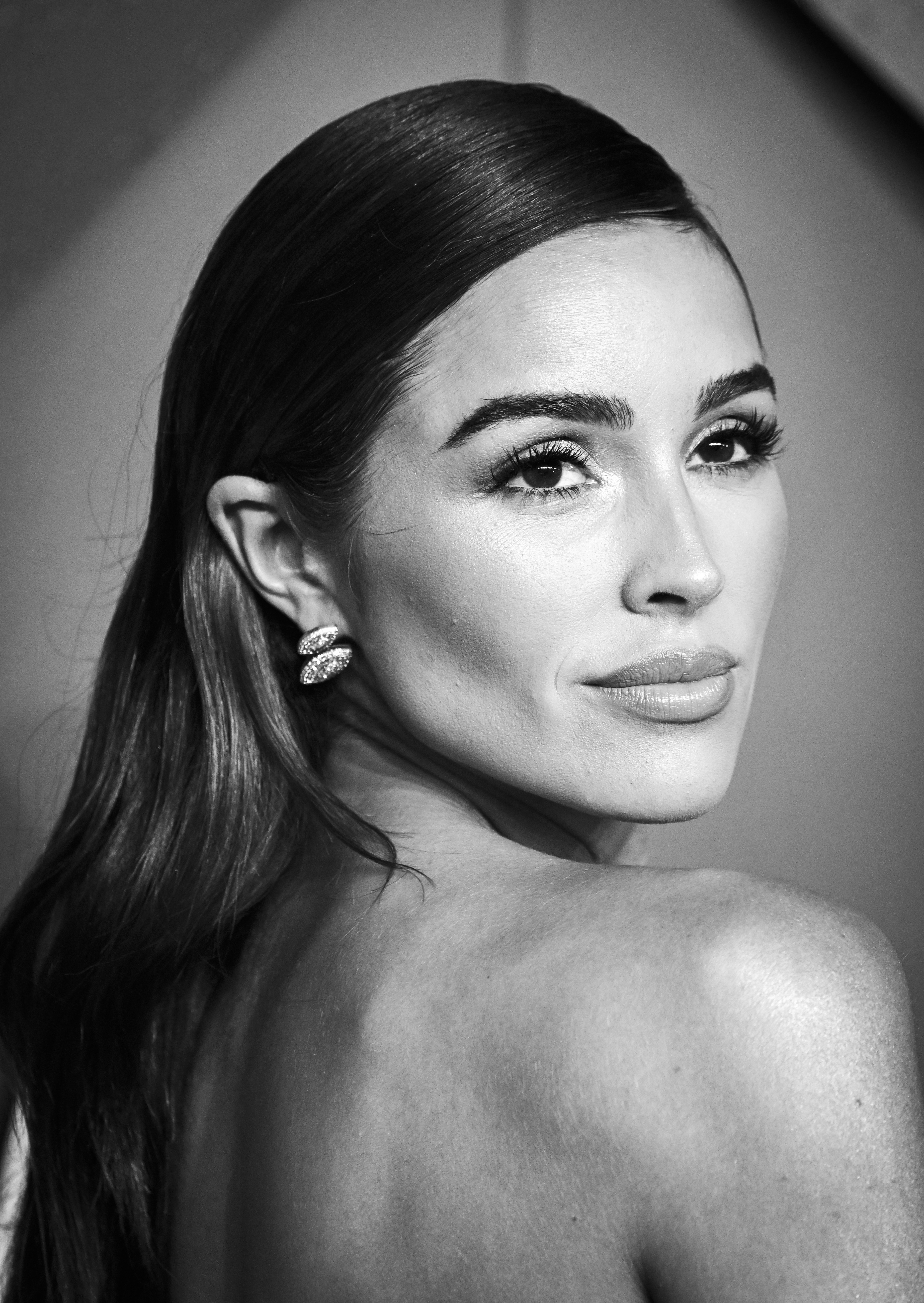 Olivia Culpo poses for the camera, wearing elegant earrings and a strapless outfit