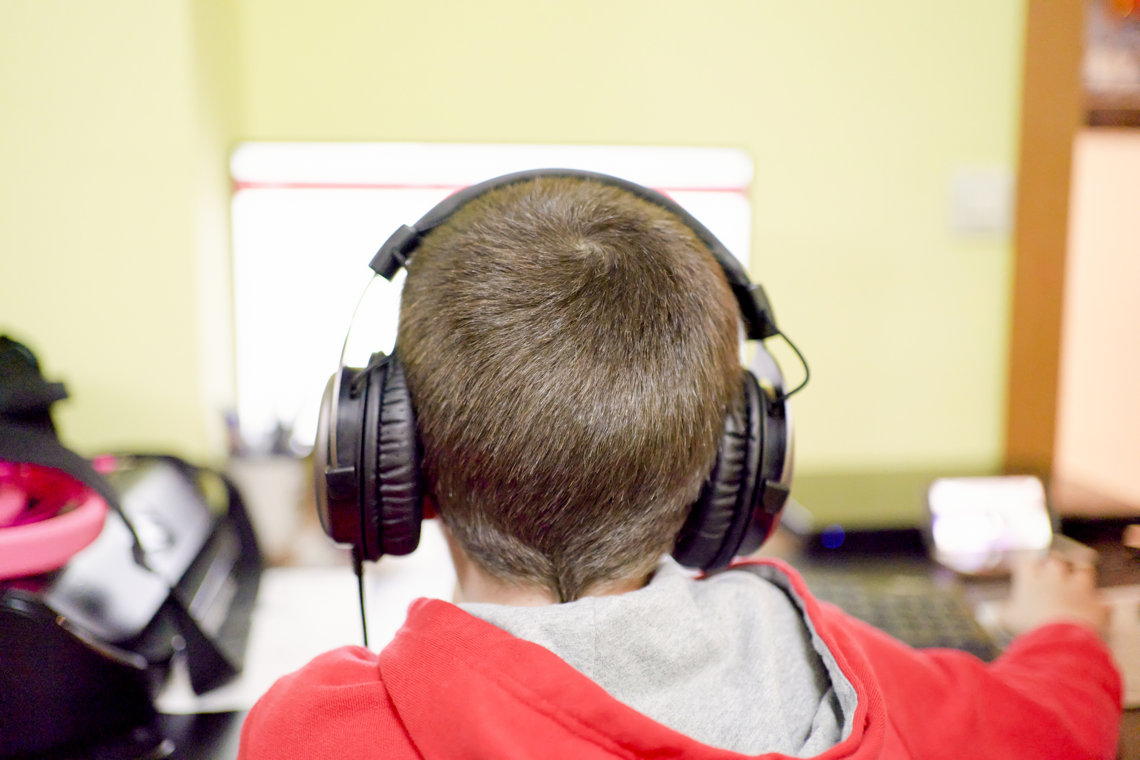 A child with short hair and large headphones sits at a desk, focused on a computer screen