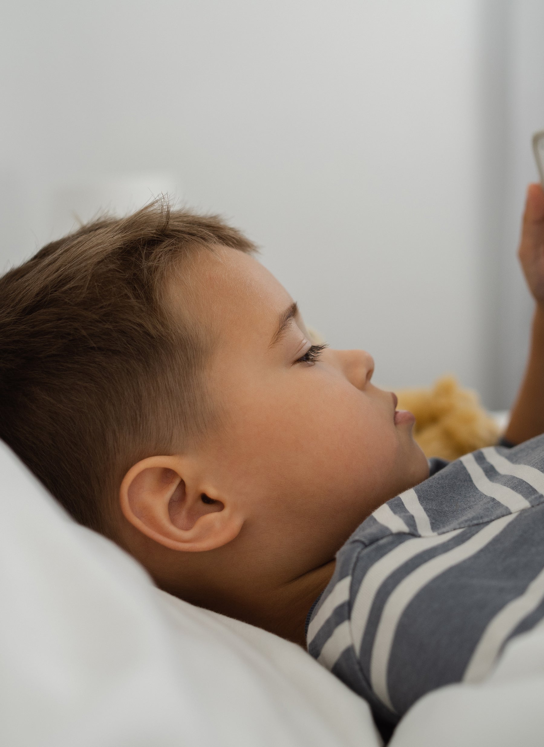 Young child in bed, holding and looking at a tablet with colorful display