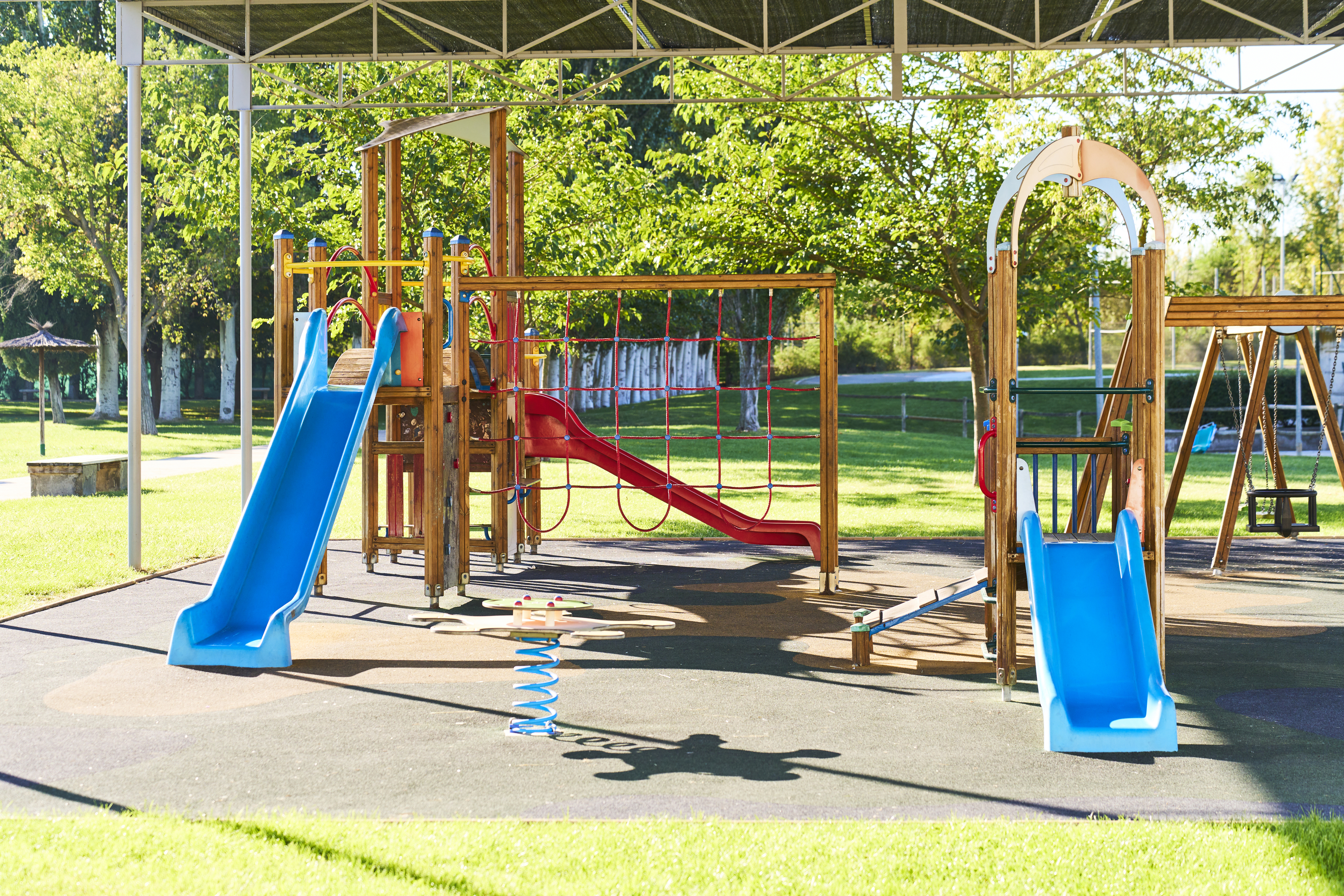 Colorful playground with various slides, climbing structures, and a spring rider under a shade structure in a park