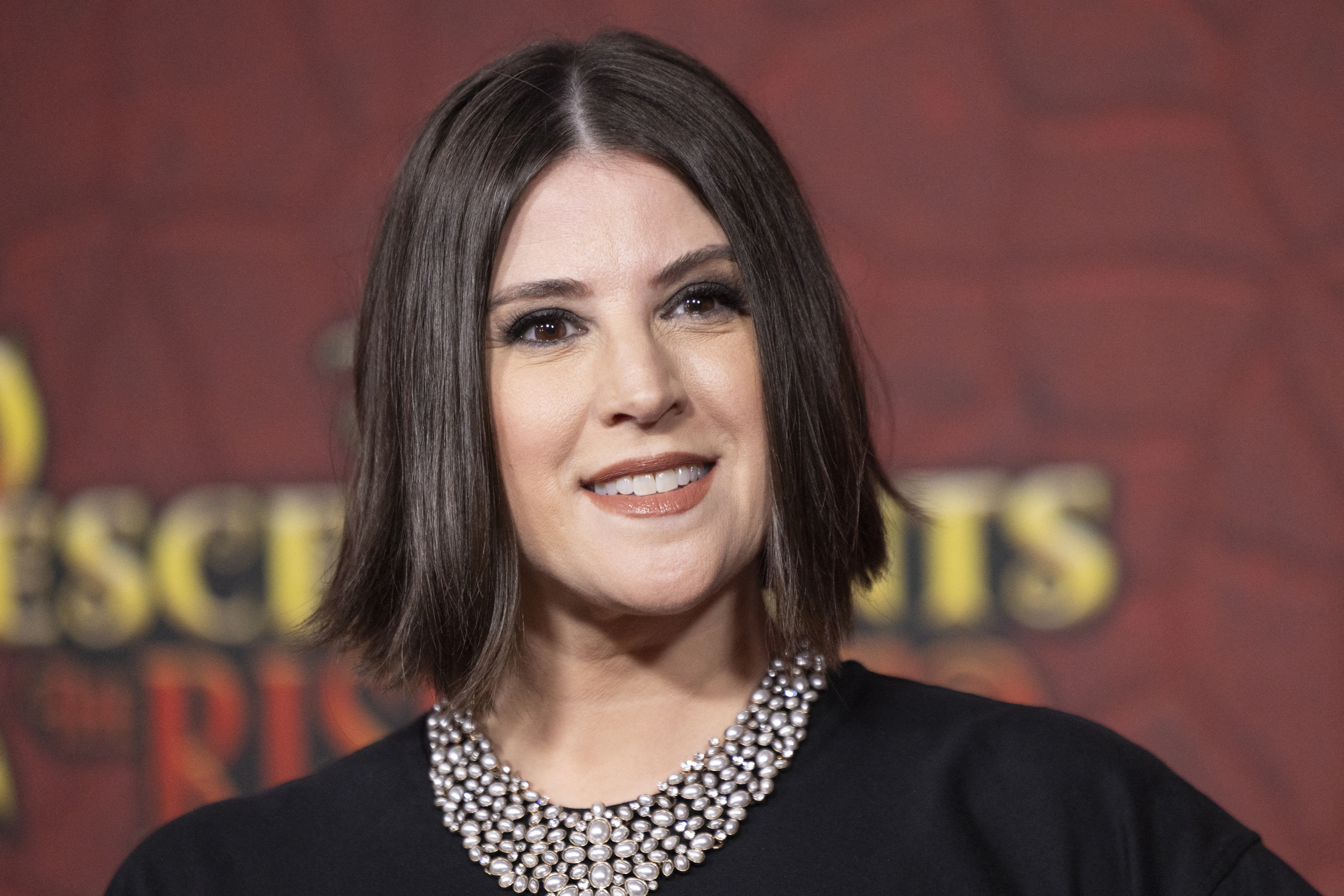Melanie Paxson on the red carpet for "Descendants: The Rise of Red" in a black outfit adorned with pearls at the neckline