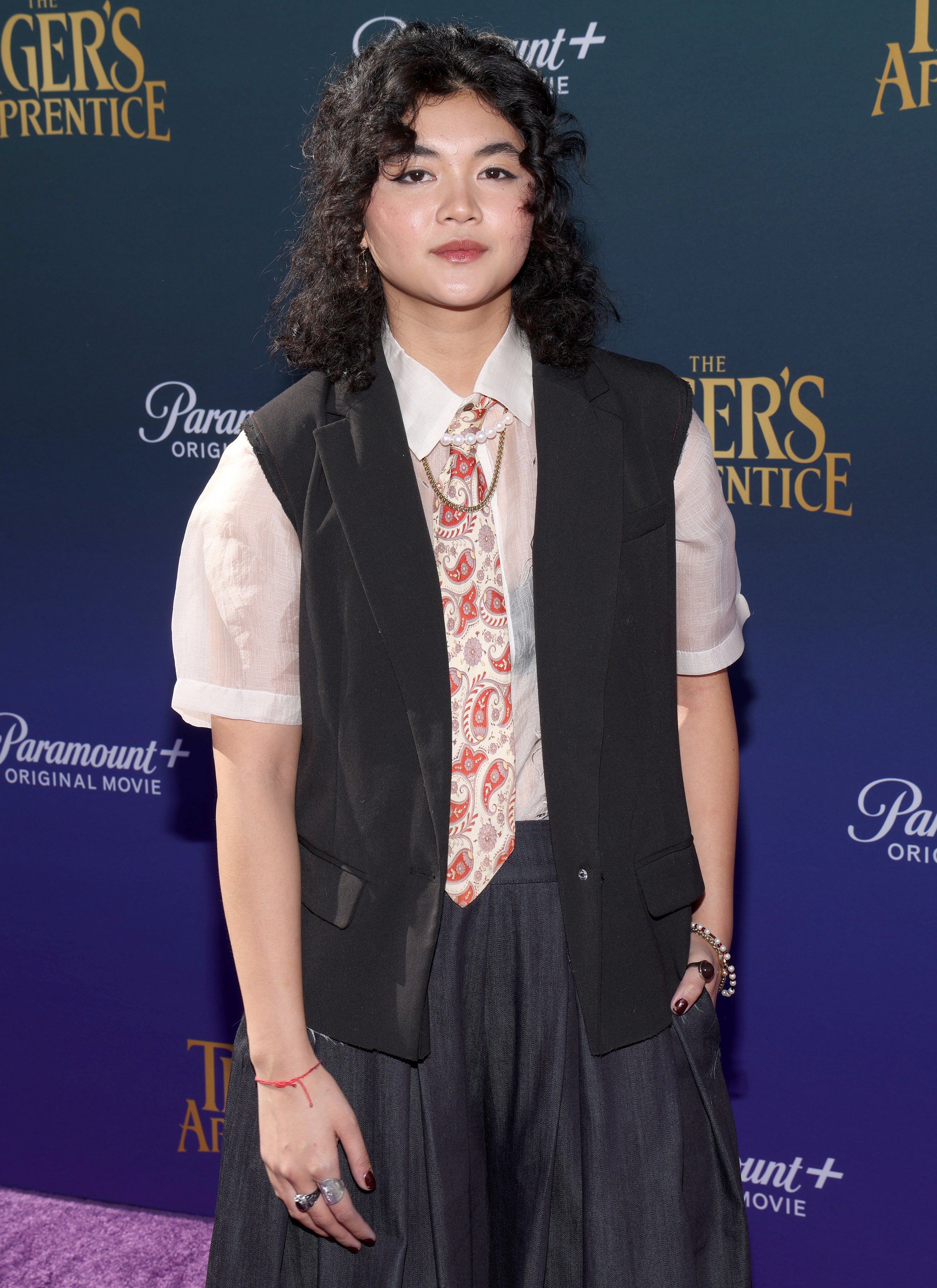 Sam Morelos on the red carpet for "The Tiger's Apprentice" in pants, a vest, sheer shirt, and tie