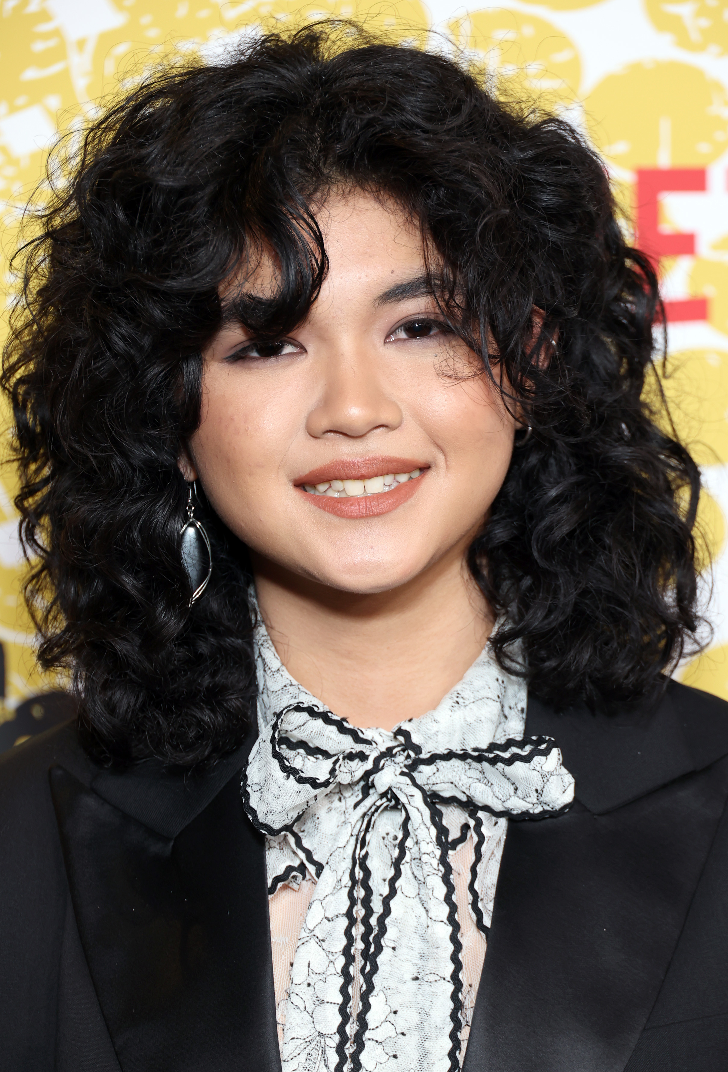 Sam Morelos at a screening reception for "That '90s Show" in a black jacket and white lace shirt with a bow
